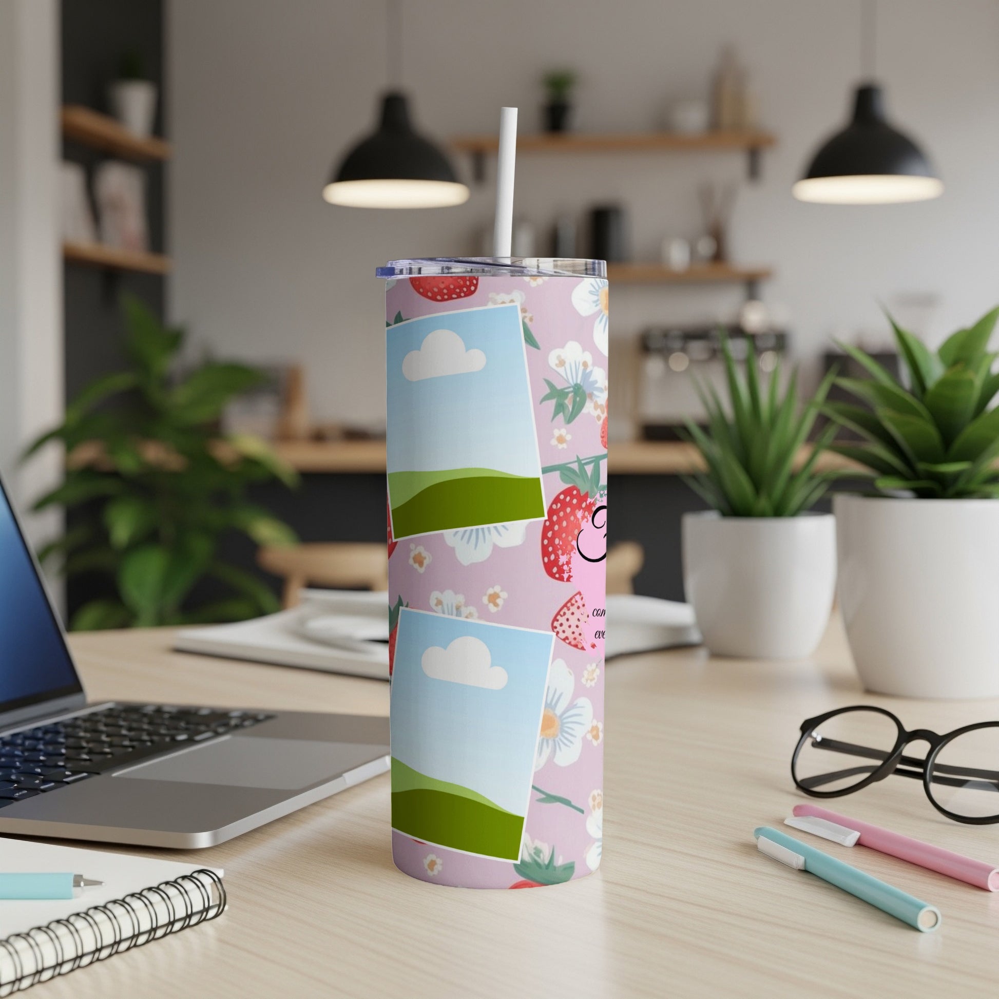 Pink tumbler with strawberries, flowers, and photos on a desk with a laptop and glasses.
