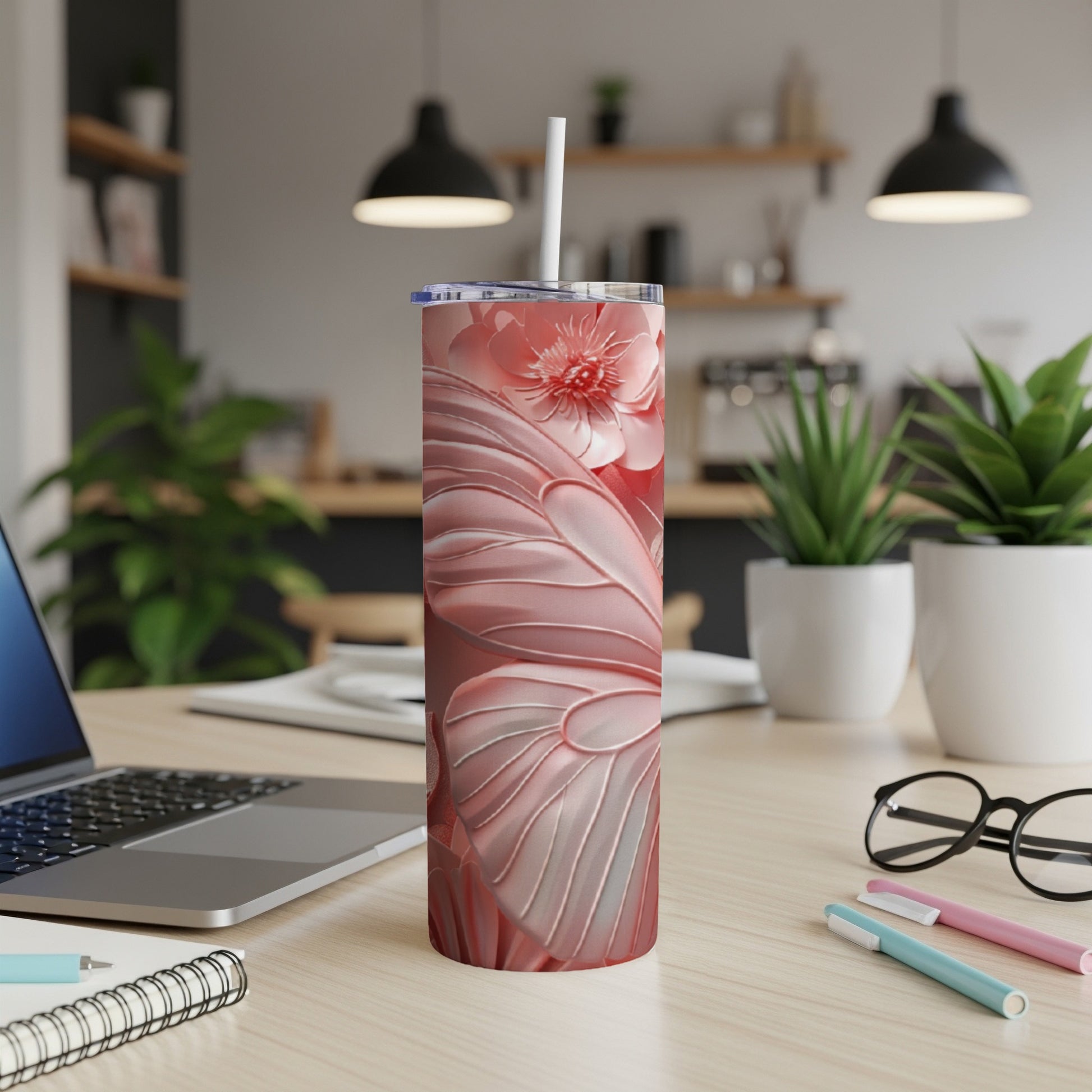 Pink floral tumbler with straw on desk with laptop and pens.