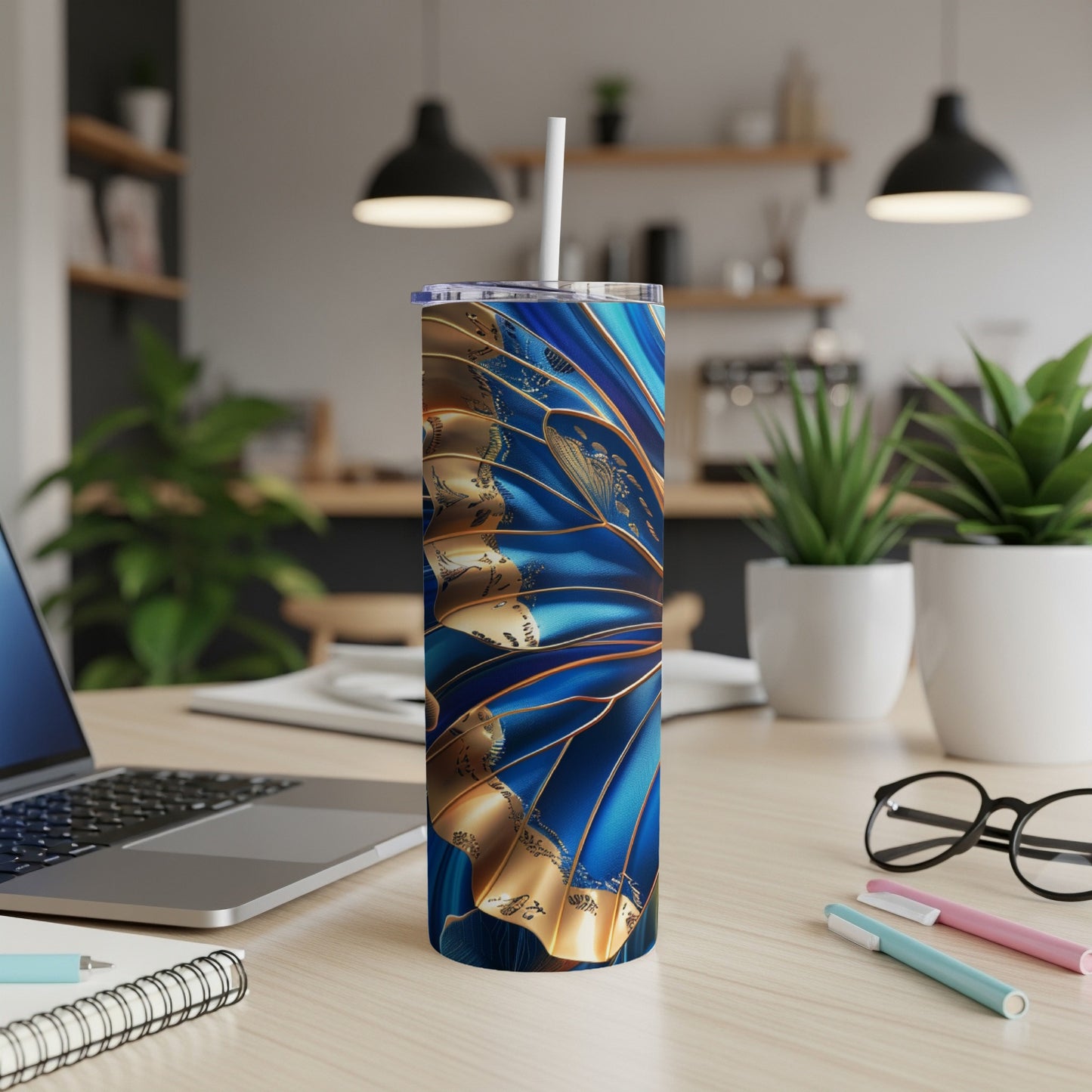 Blue and gold abstract patterned tumbler with straw on a desk.