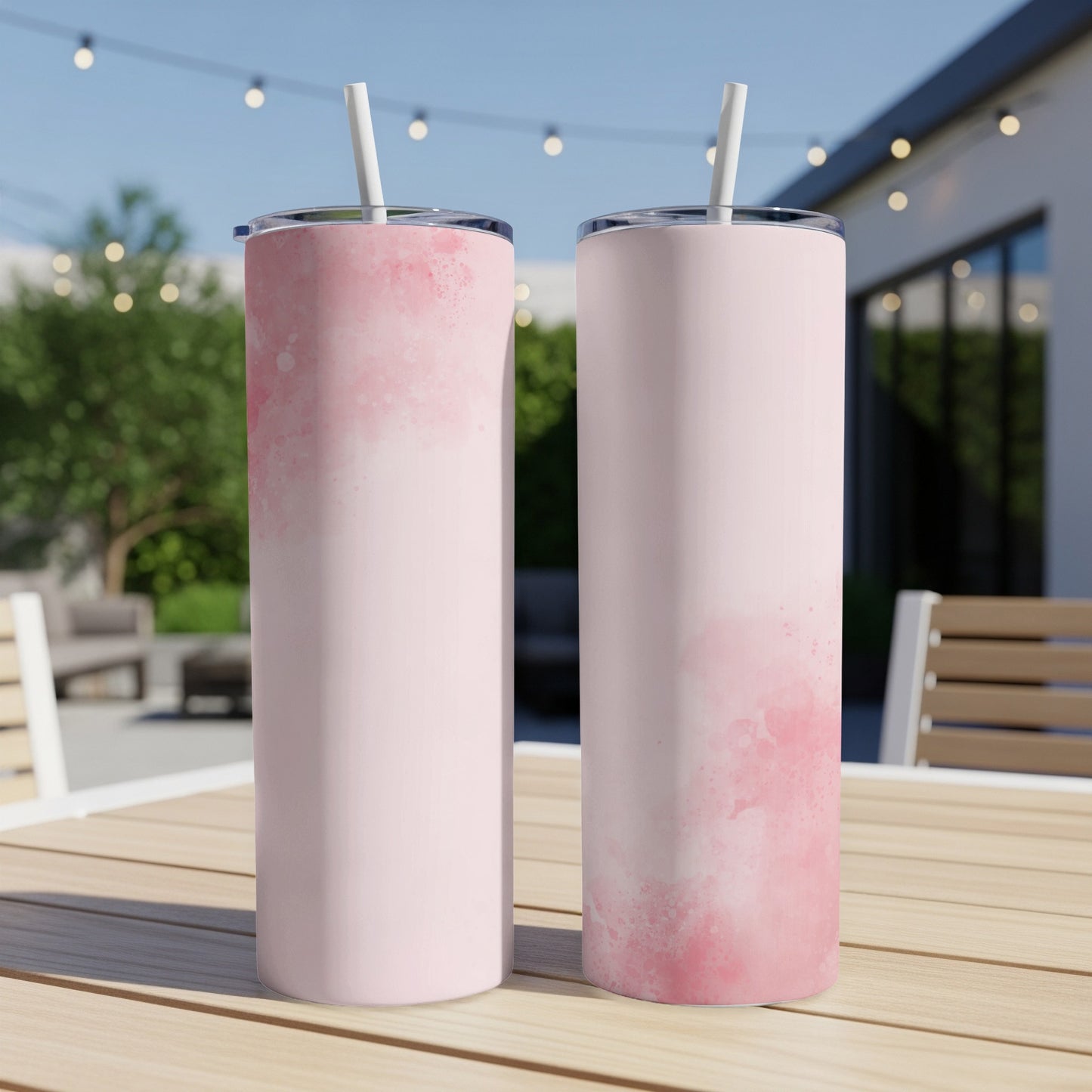 Two pink watercolor print tumblers with straws on a wooden table.