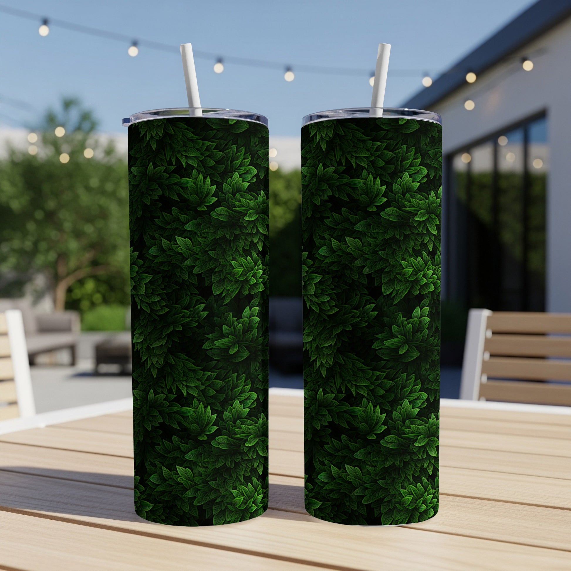 Two green leaf-patterned tumblers with straws sit on a wooden table.