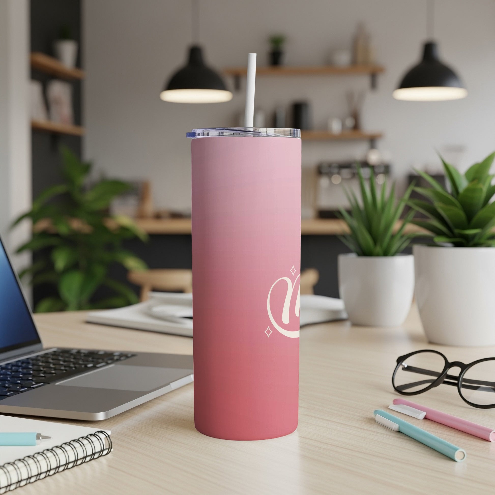 Pink gradient tumbler with white heart design and straw on desk.