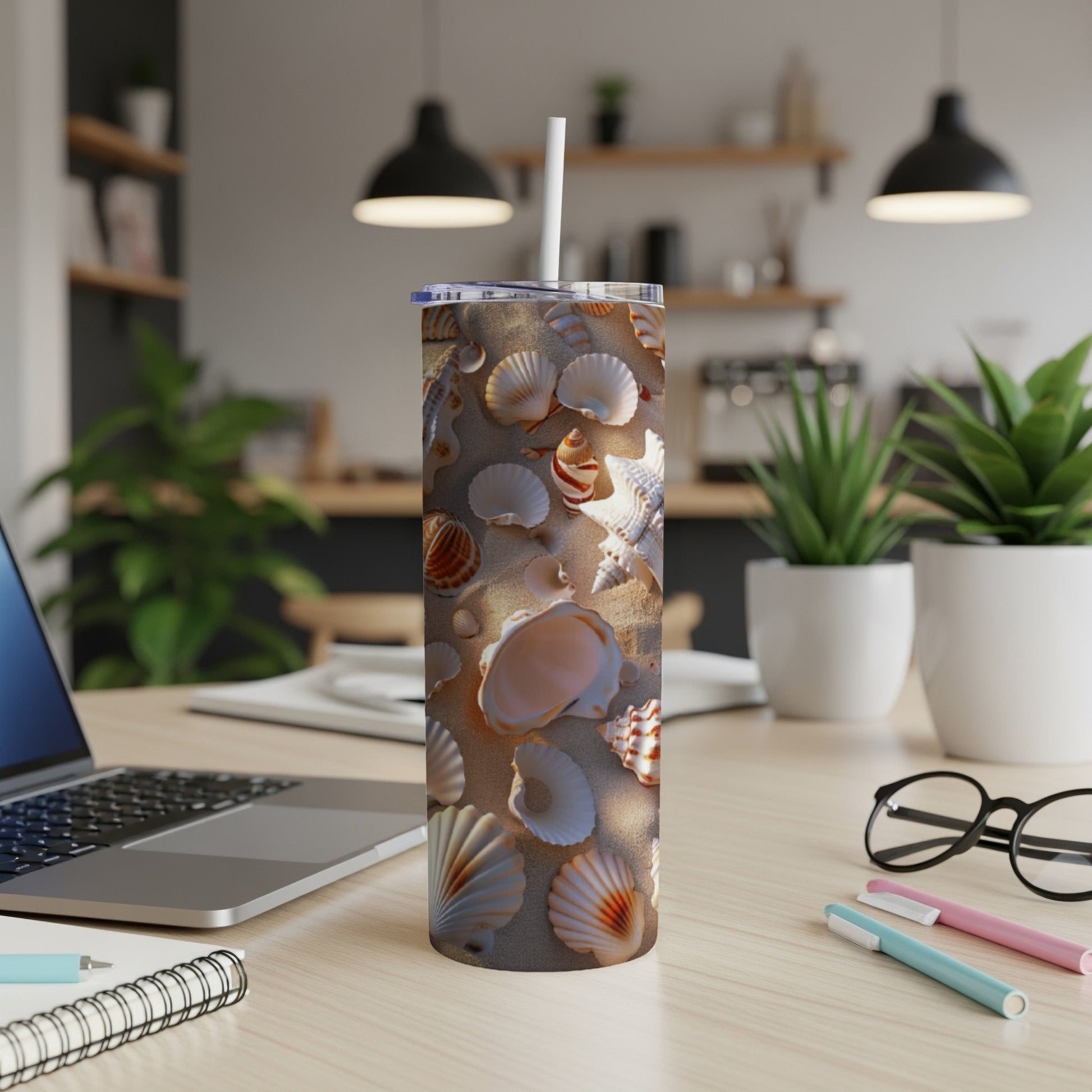 Tumbler cup with seashell pattern on a desk with laptop and pens.