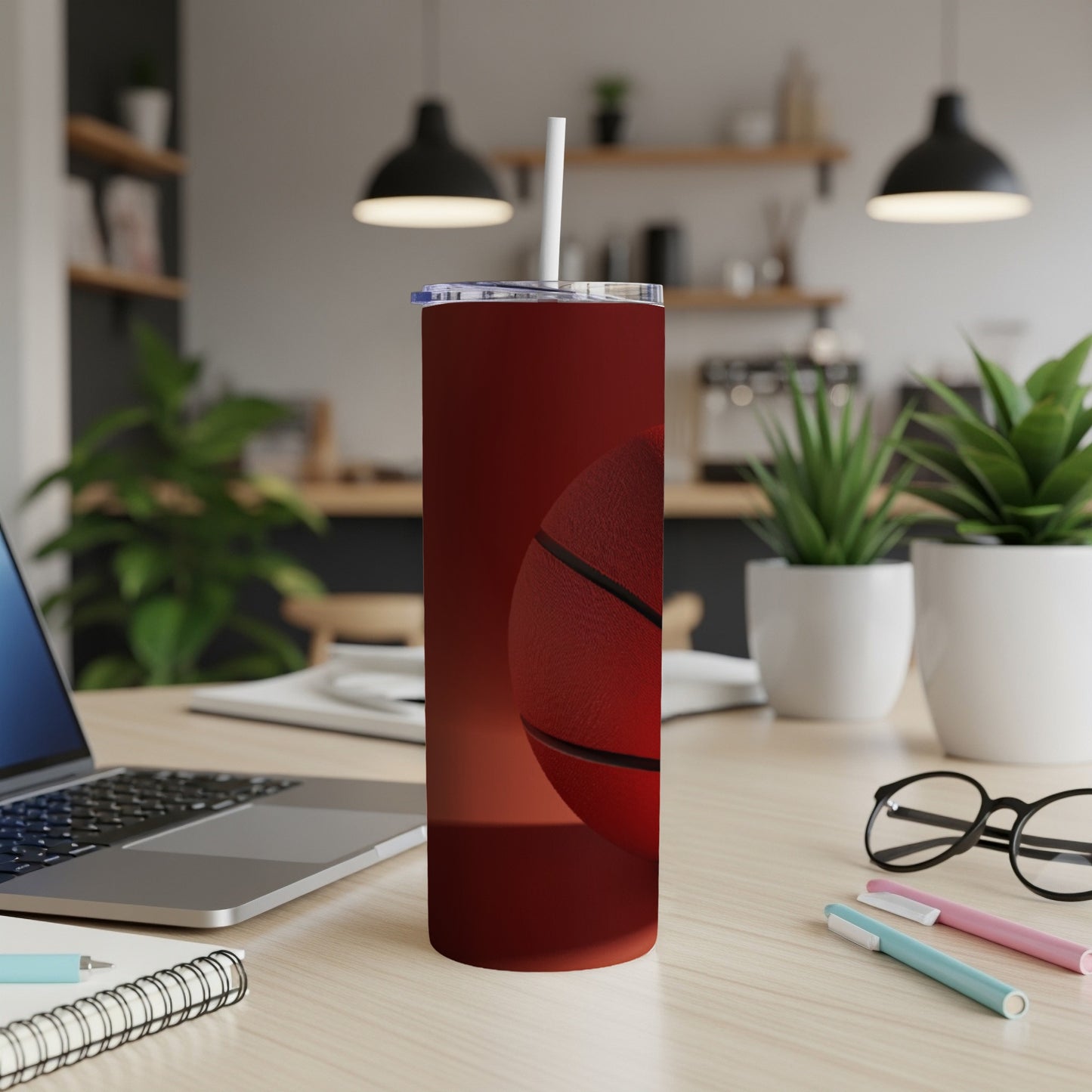 Red basketball tumbler with straw on a desk next to a laptop.