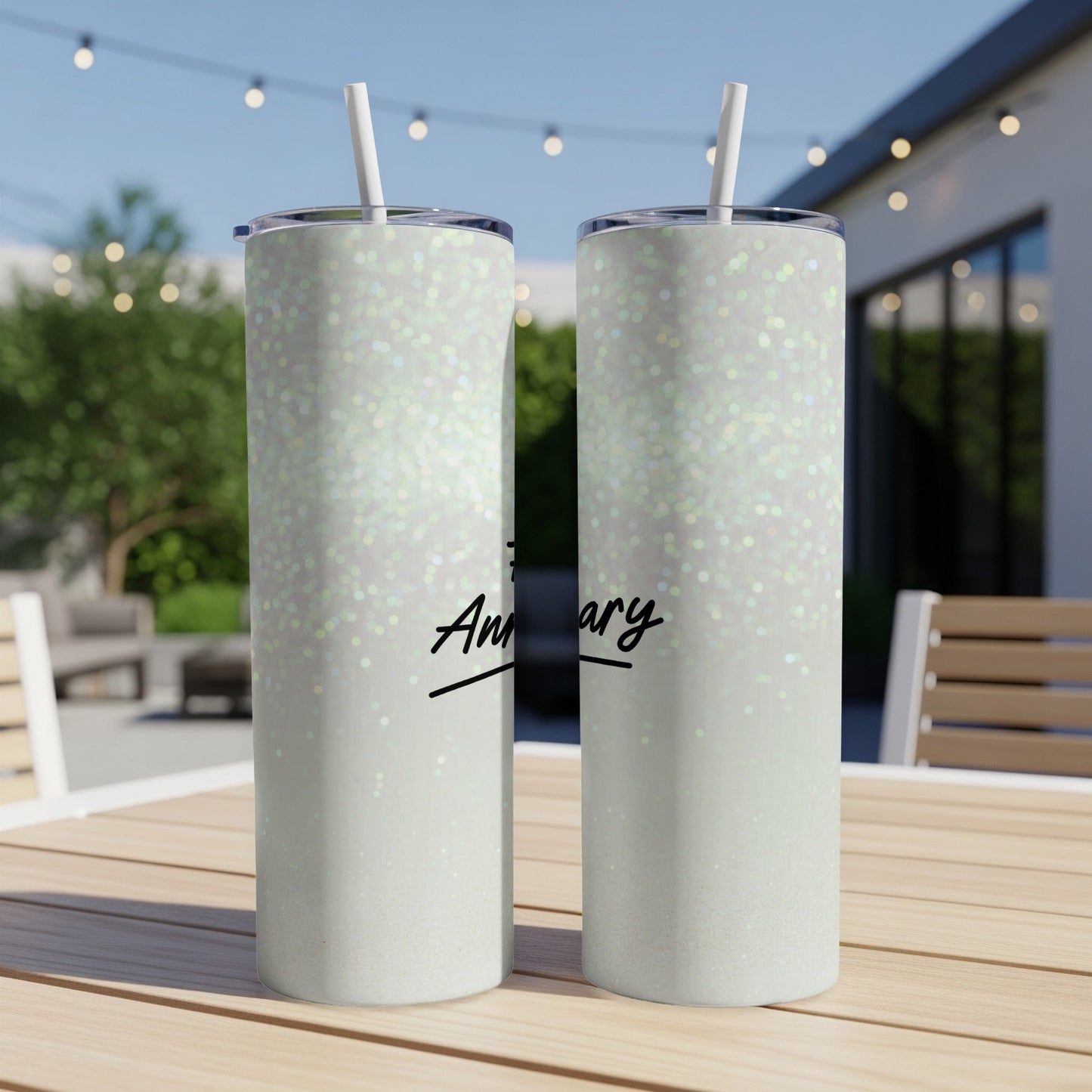 Two glittery tumblers with "Anniversary" text sit on an outdoor table.