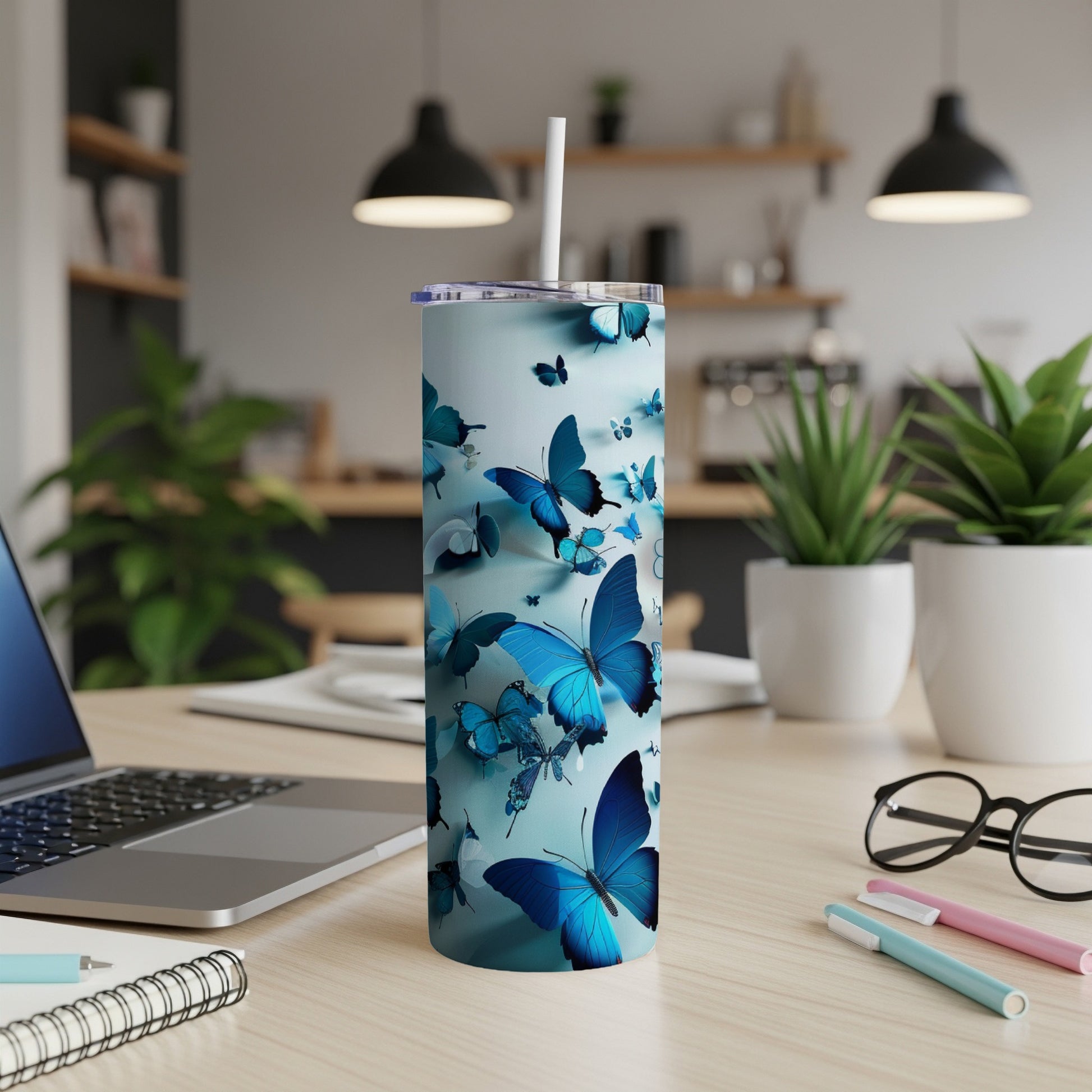 Blue butterfly tumbler with straw on a desk with a laptop and pens.