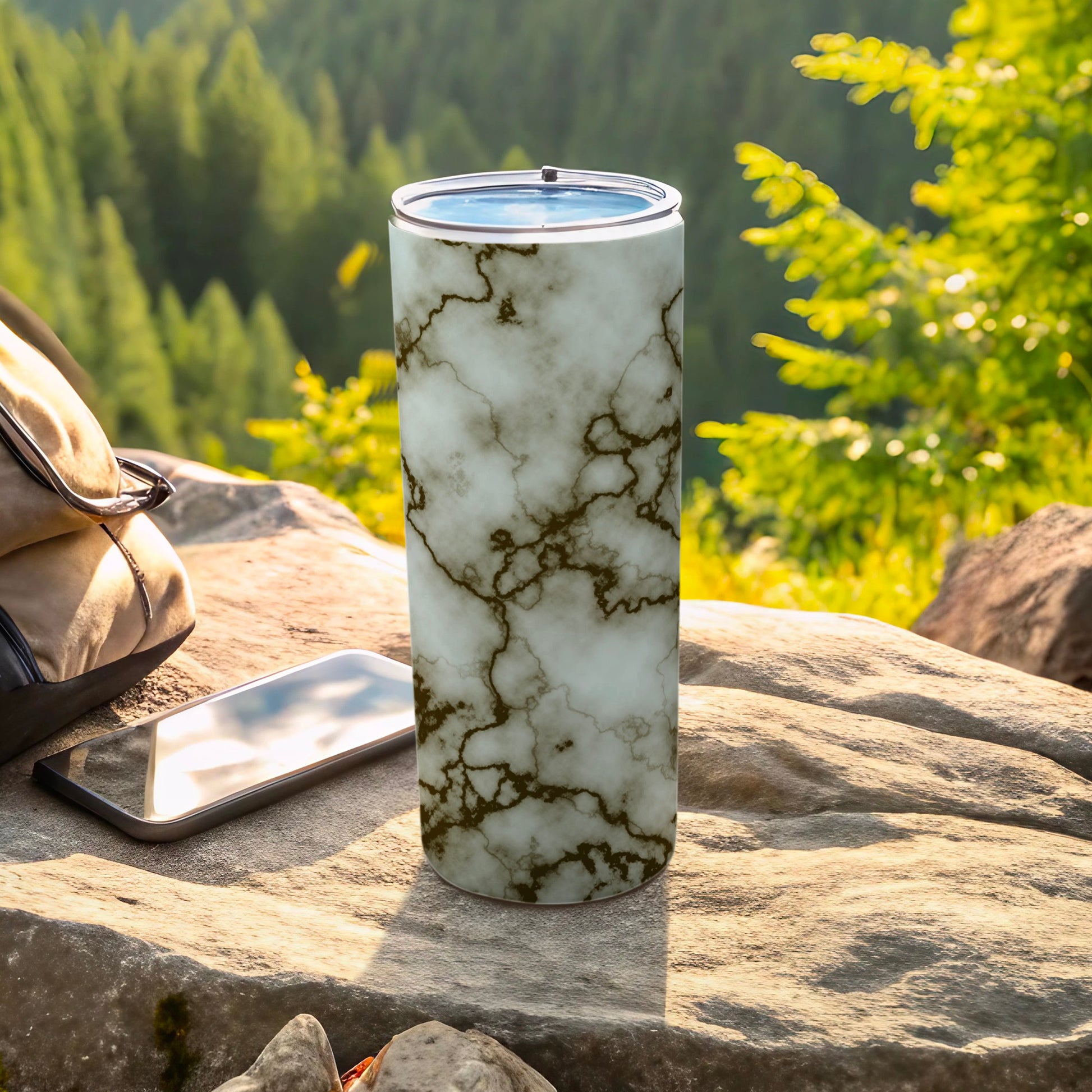 Marble print tumbler on rock with phone and backpack outdoors.