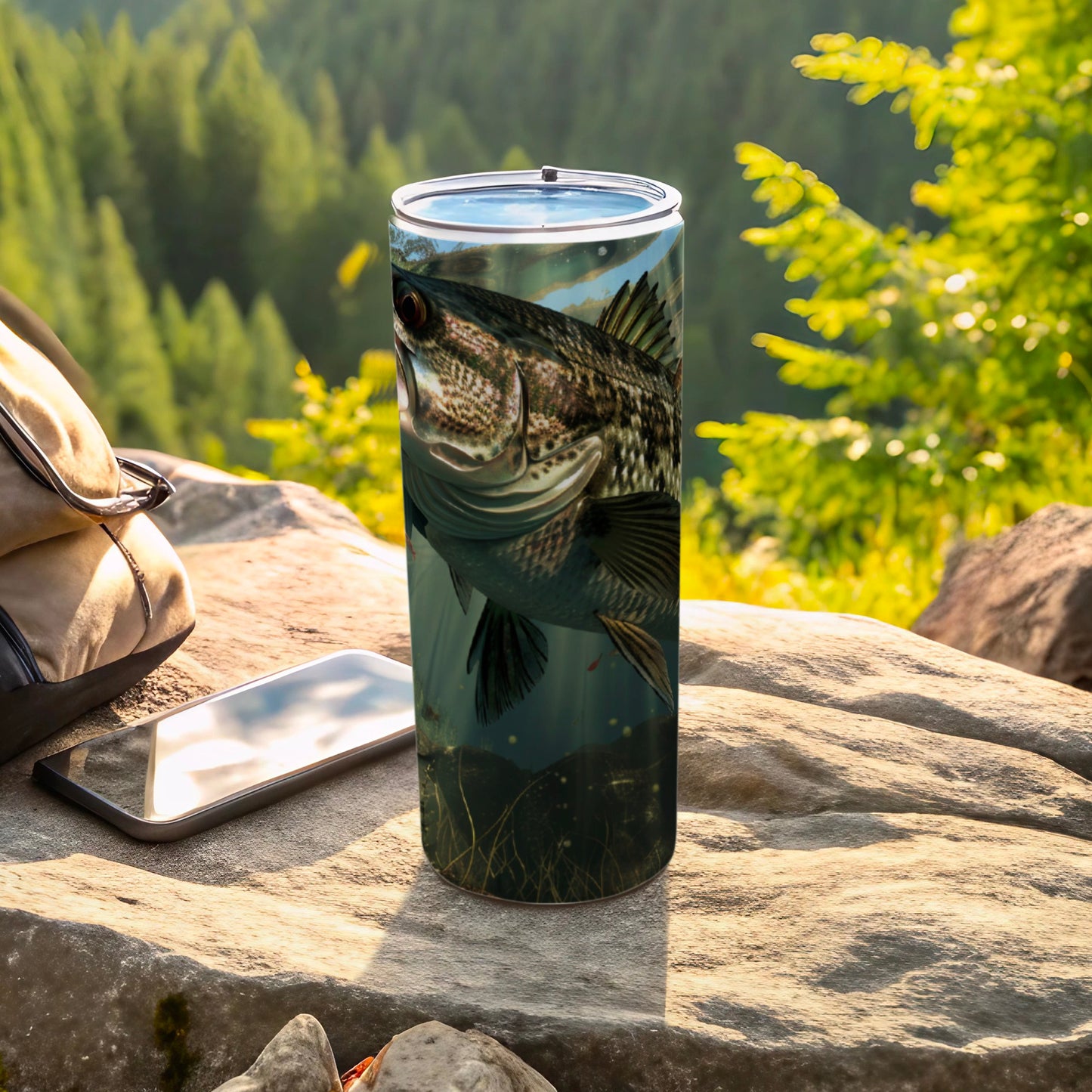 Fishing tumbler with realistic bass image, outdoors on rock next to phone.