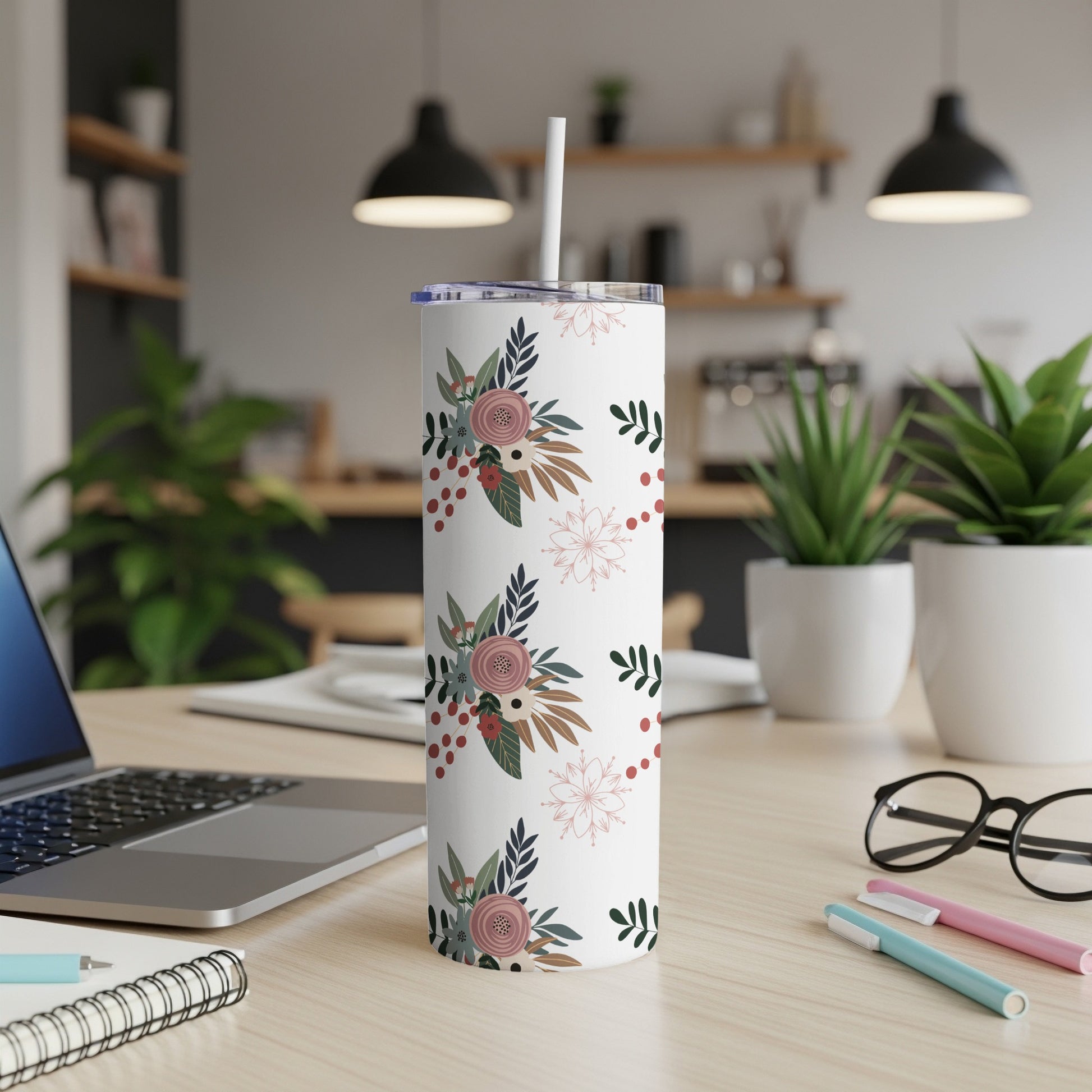 White tumbler with floral and snowflake pattern, straw, on a desk.