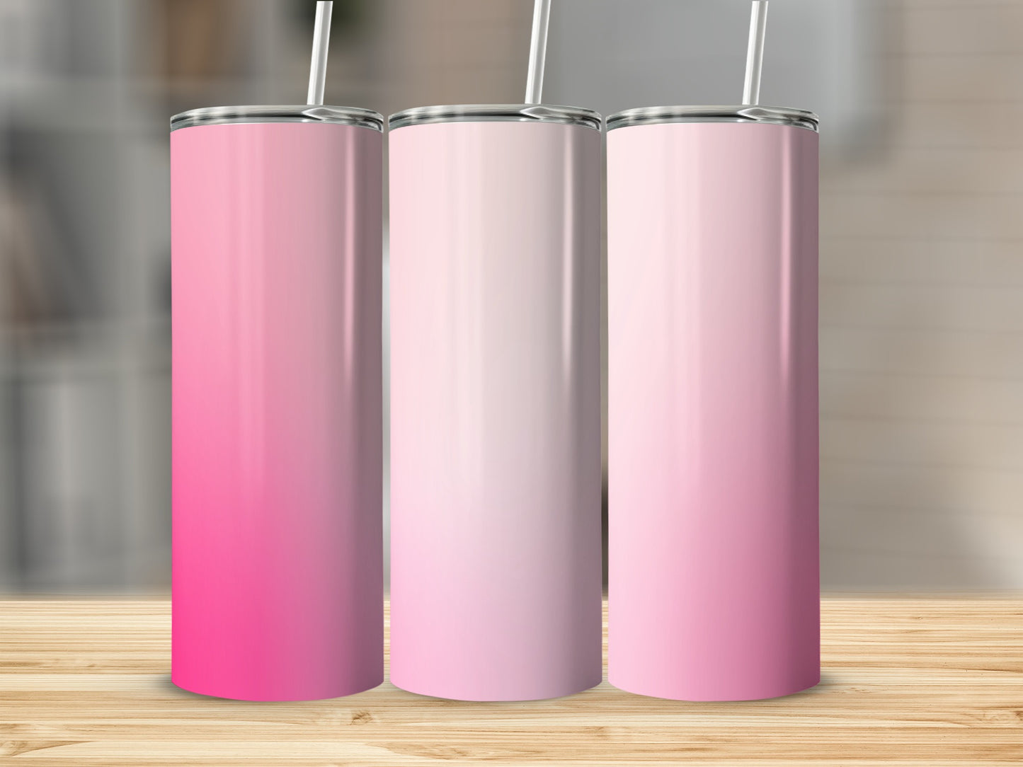 Three gradient pink tumblers with straws on a wooden surface.