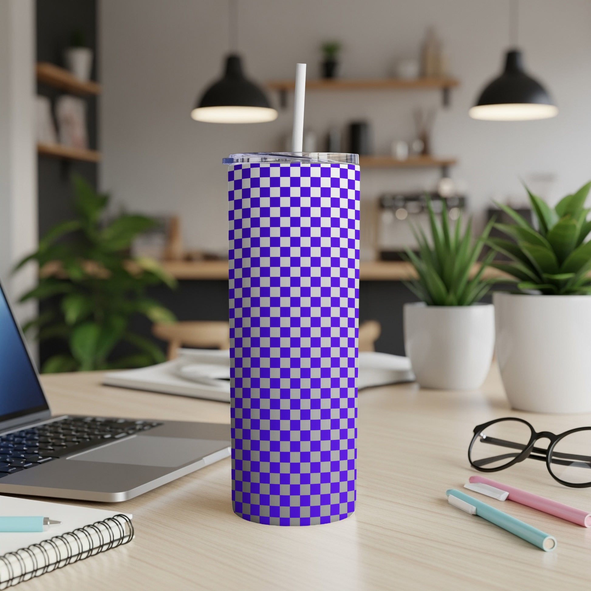 Blue and white checkered tumbler with straw on desk next to laptop.