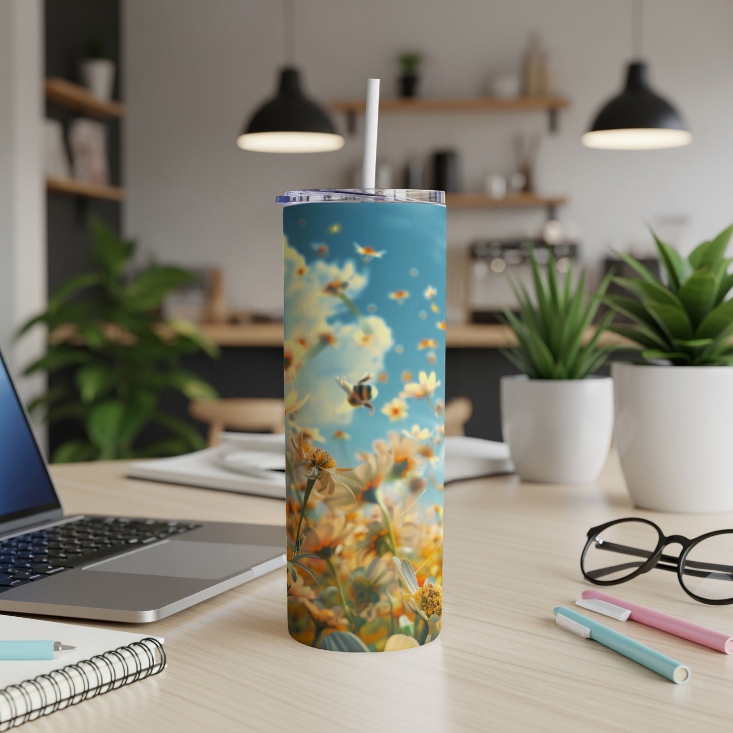 Tumbler with bees and sunflowers against a blue sky, on a desk.