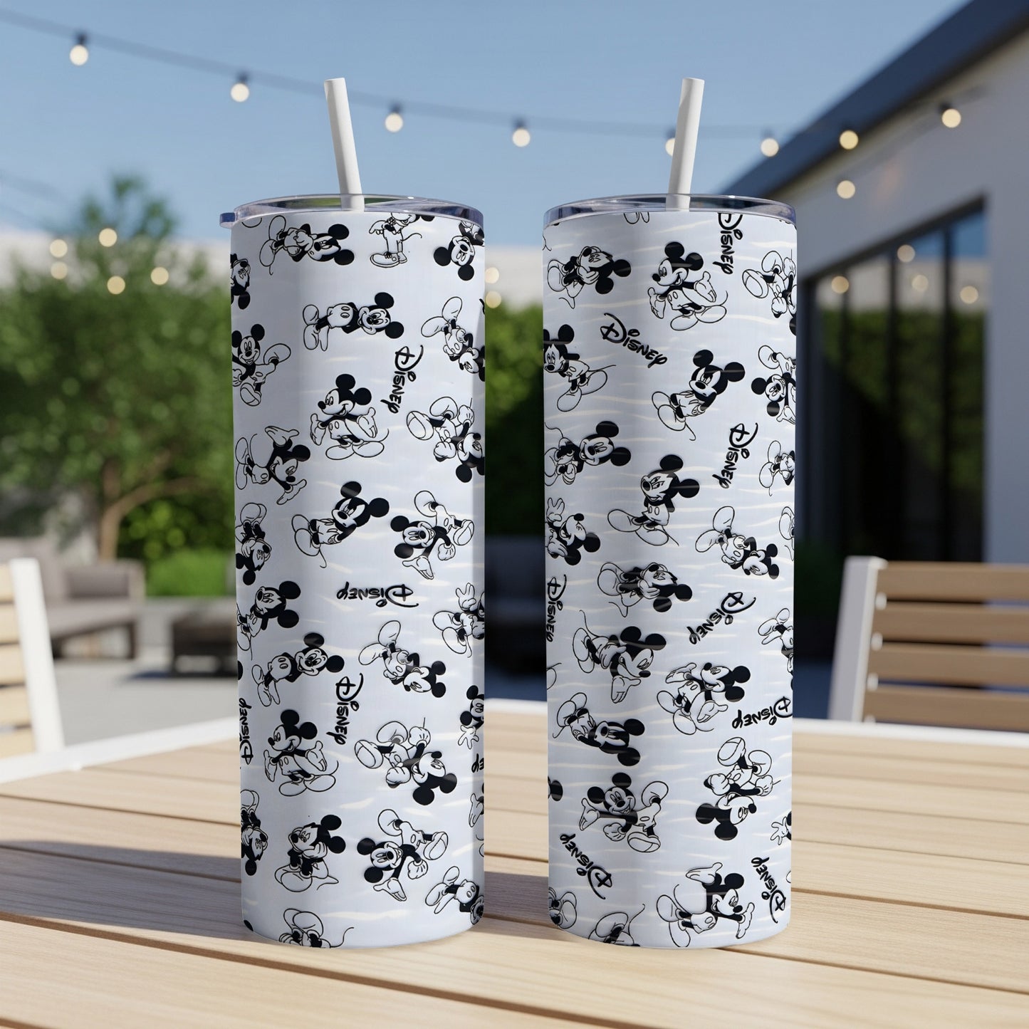 Two Mickey Mouse patterned tumblers with straws on a wooden table.