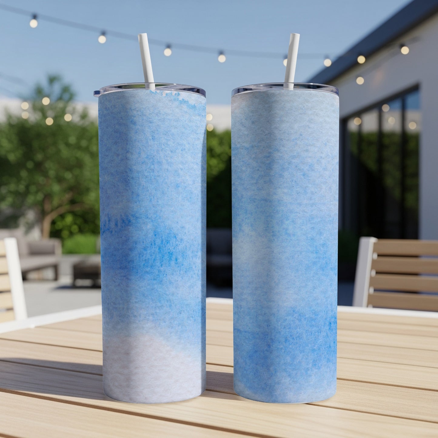 Two blue watercolor patterned tumblers with straws on a wooden table.