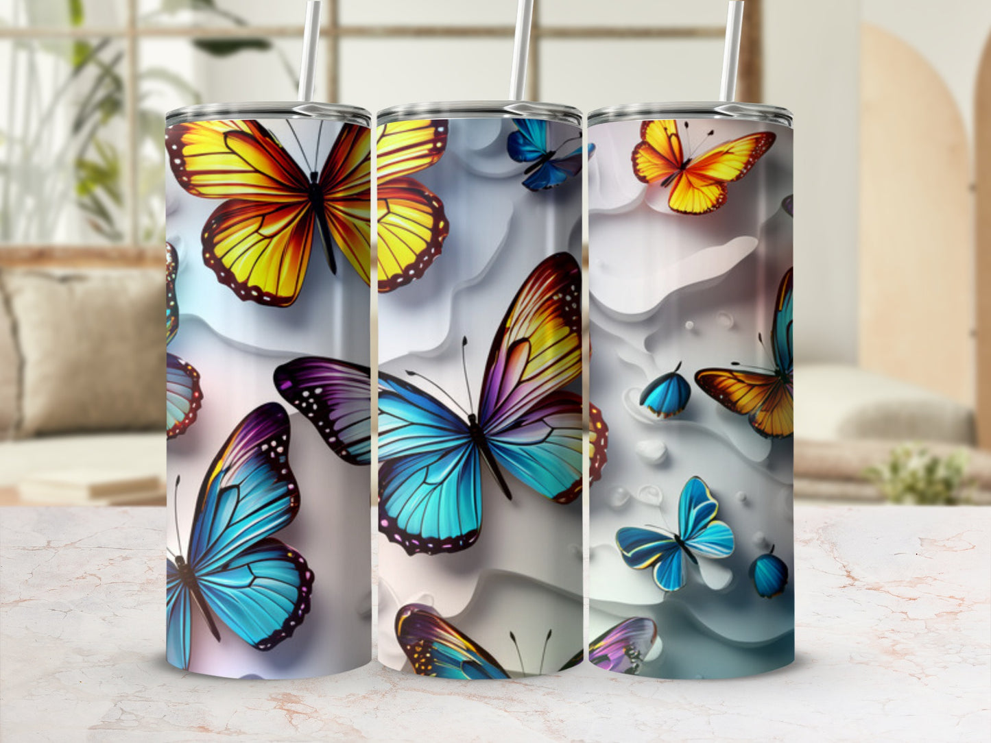 Three colorful butterfly-themed tumblers with straws on a marble surface.