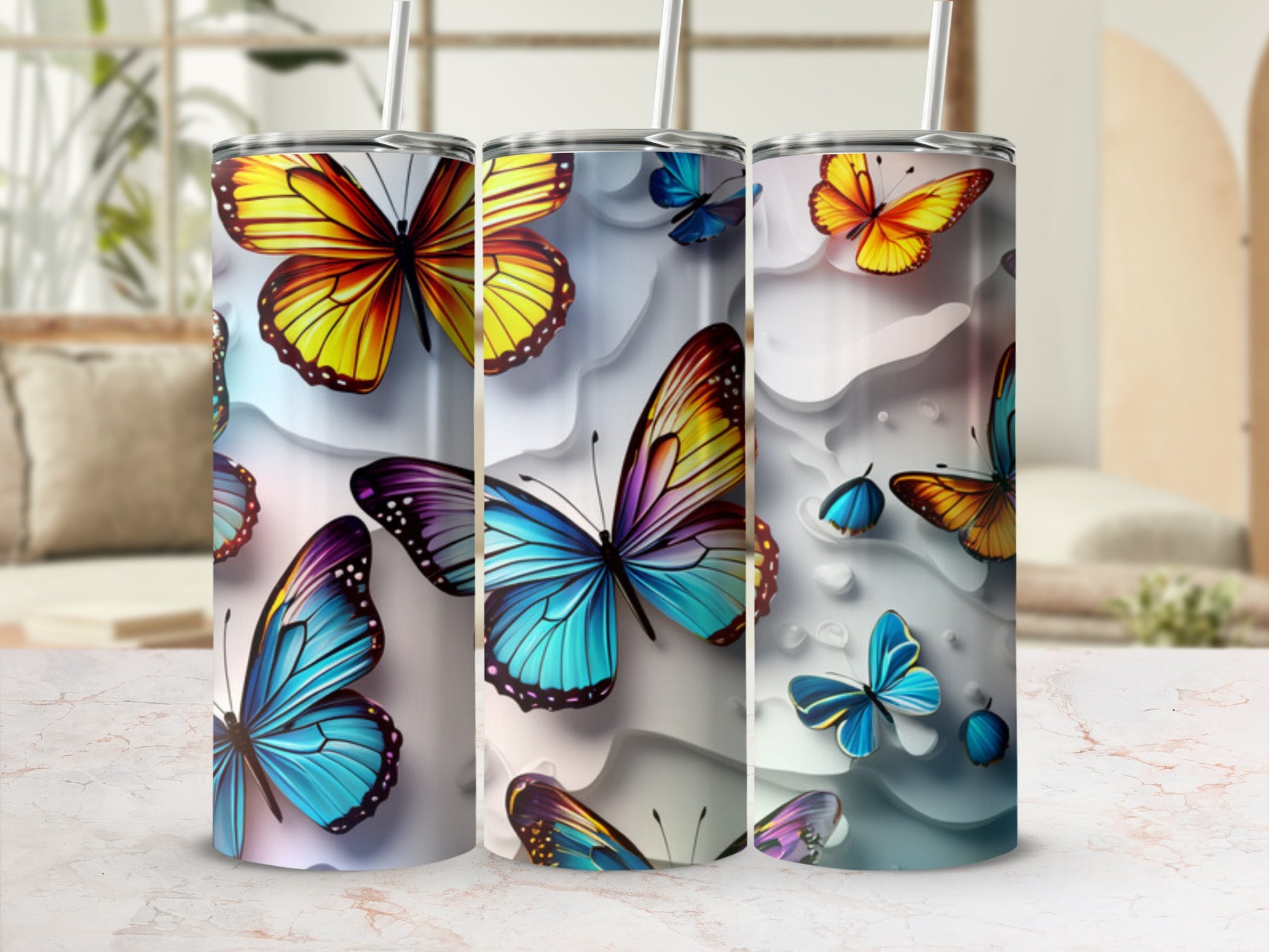 Three colorful butterfly-themed tumblers with straws on a marble surface.