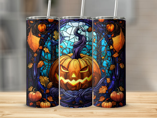 Stained glass pumpkin on a tumbler, surrounded by autumn leaves and branches.