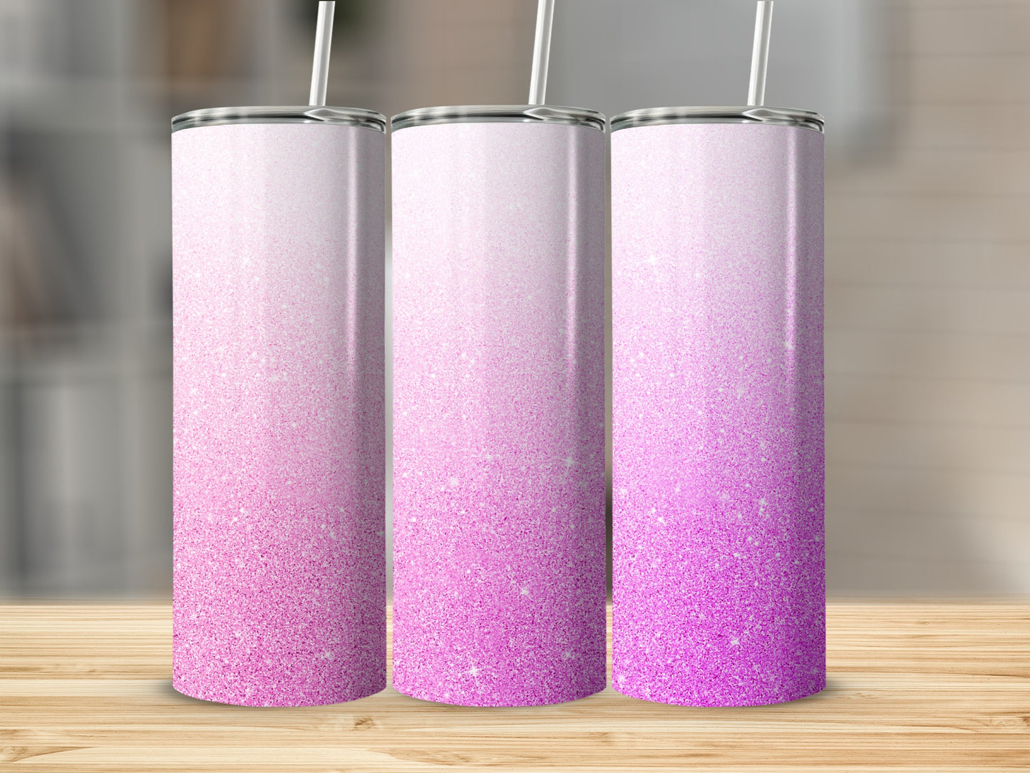 Three glittery pink ombre tumblers with straws on a wooden surface.