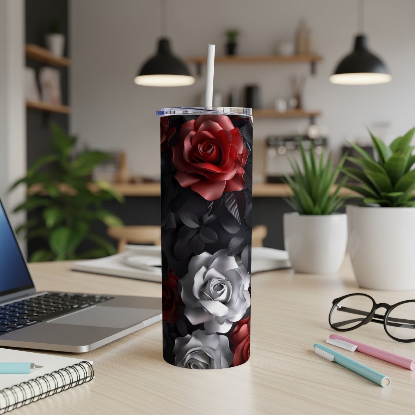 Tumbler with red and white roses on dark background, on desk with laptop.
