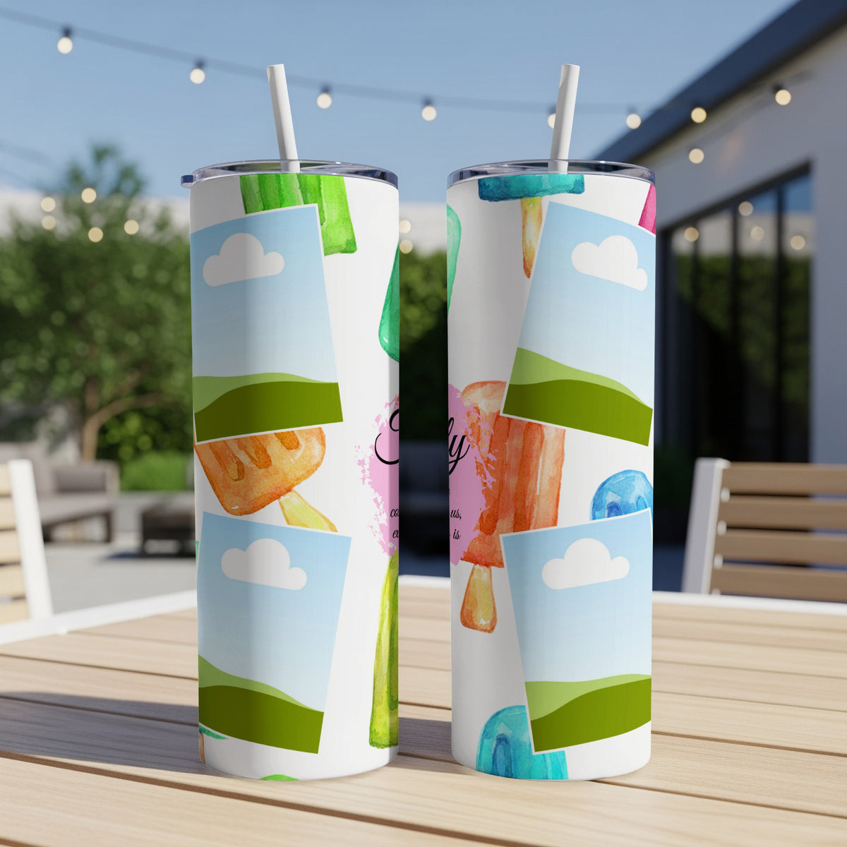 Tumblers with watercolor popsicle and cloud designs on a table outdoors.