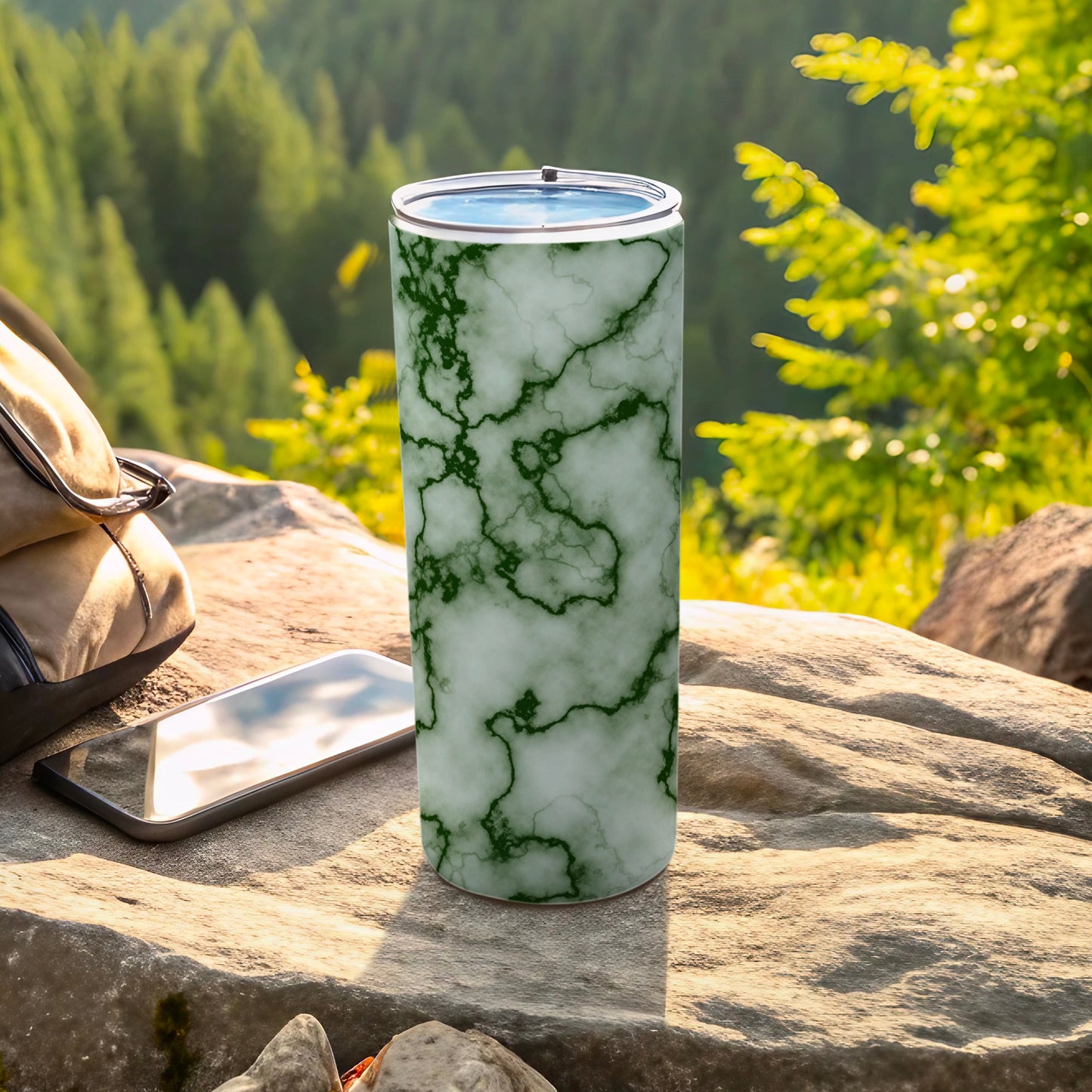 Green and white marble pattern tumbler with phone and backpack on rocks.