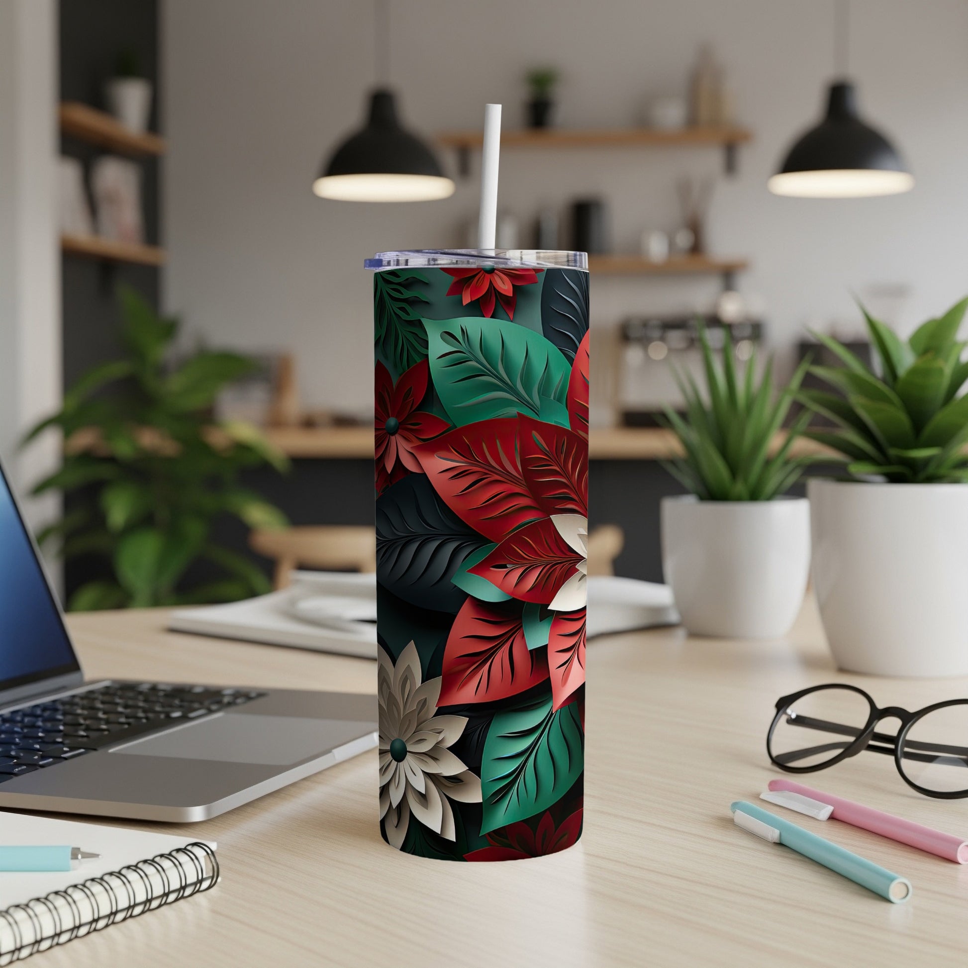 Tall tumbler with poinsettia floral pattern, straw, on desk.