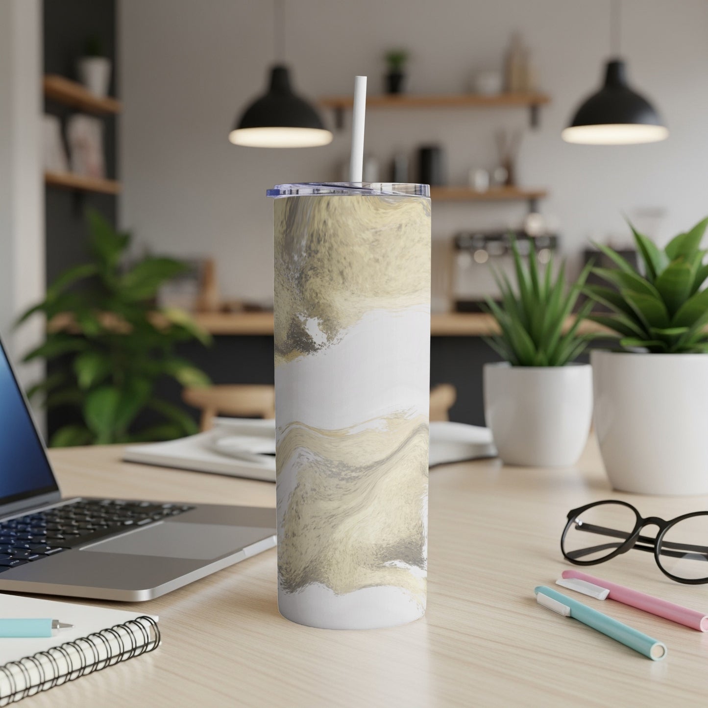 White and gold marbled tumbler with straw on a desk.