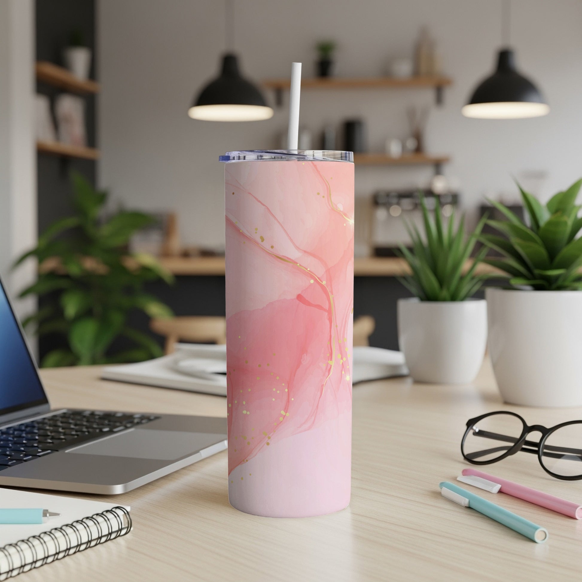 Pink marble tumbler with gold accents and a white straw on a desk.