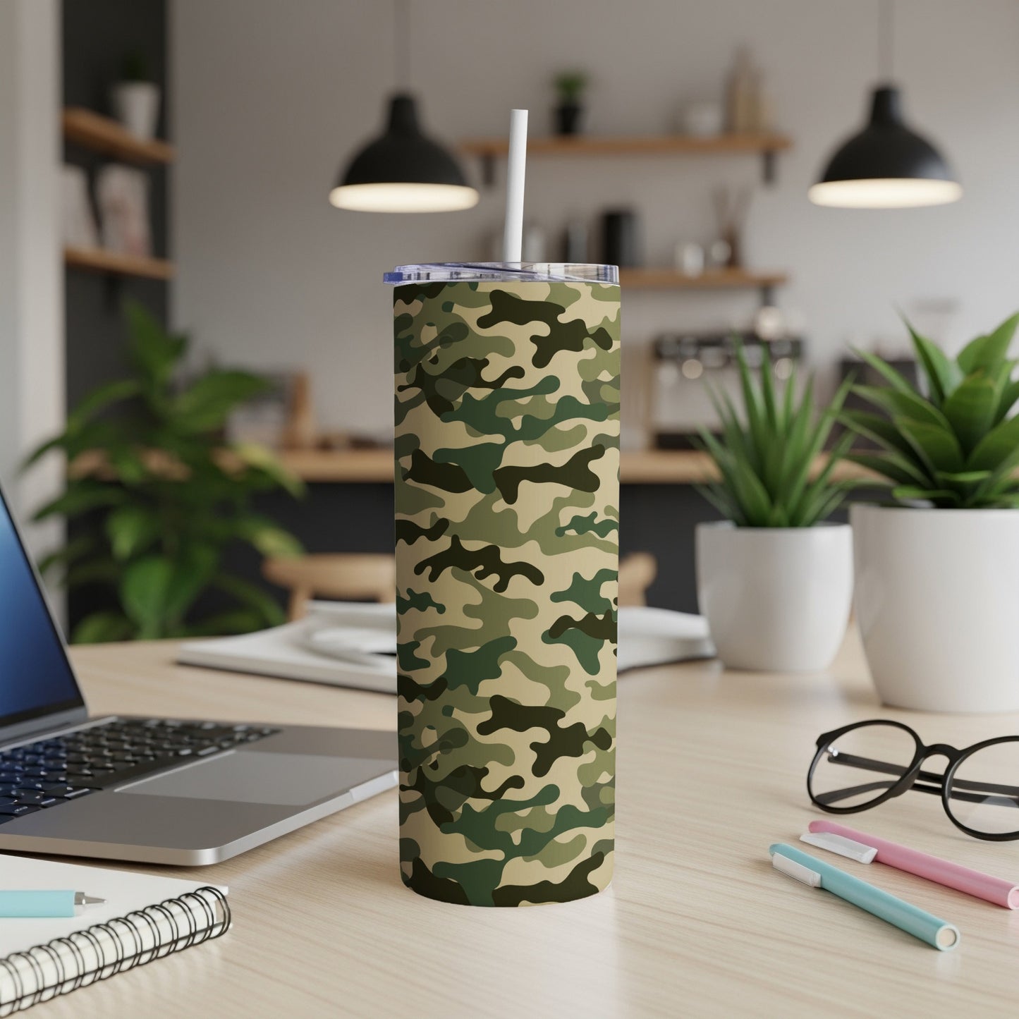 Tumbler with camouflage pattern and straw sits on a wooden desk with laptop.