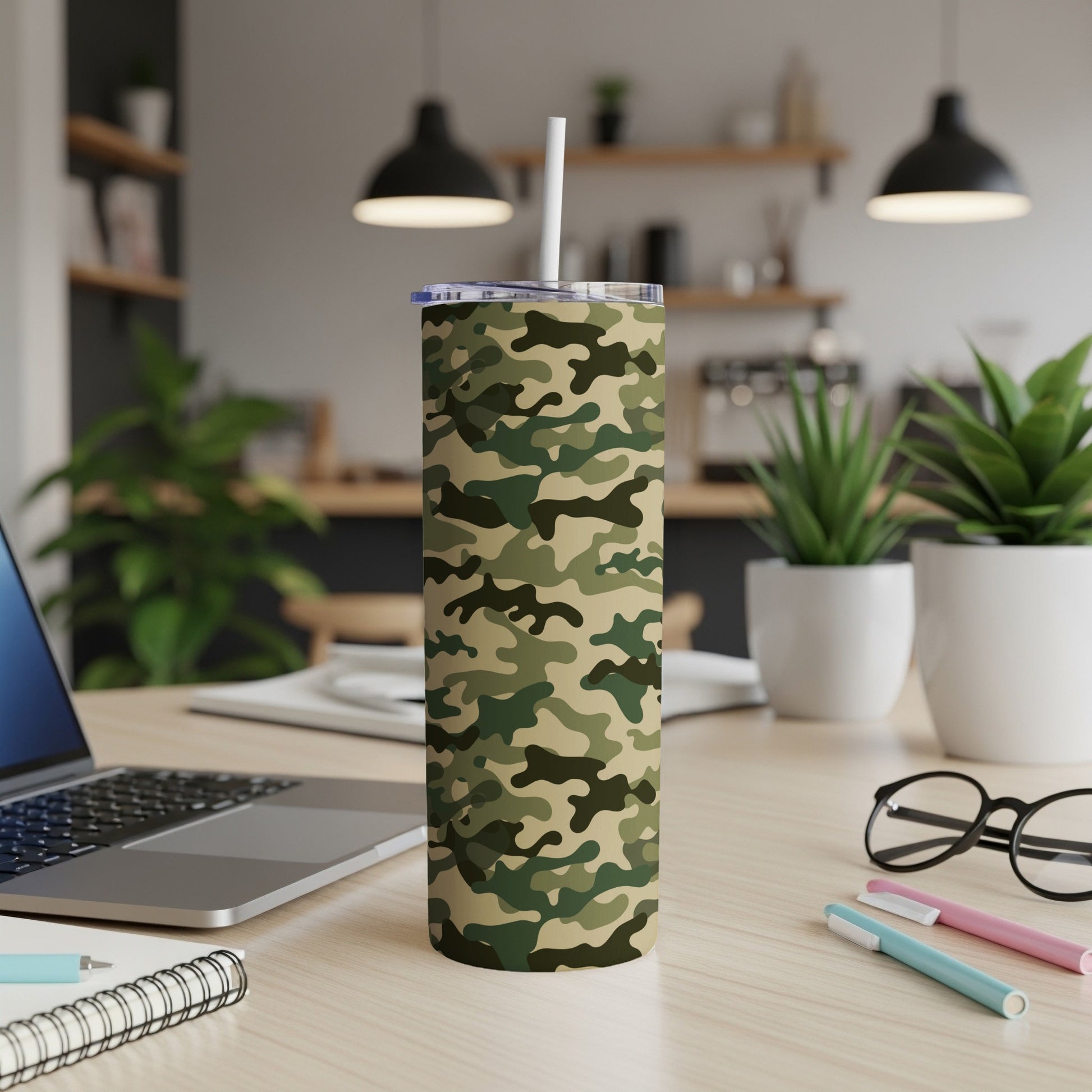 Tumbler with camouflage pattern and straw sits on a wooden desk with laptop.
