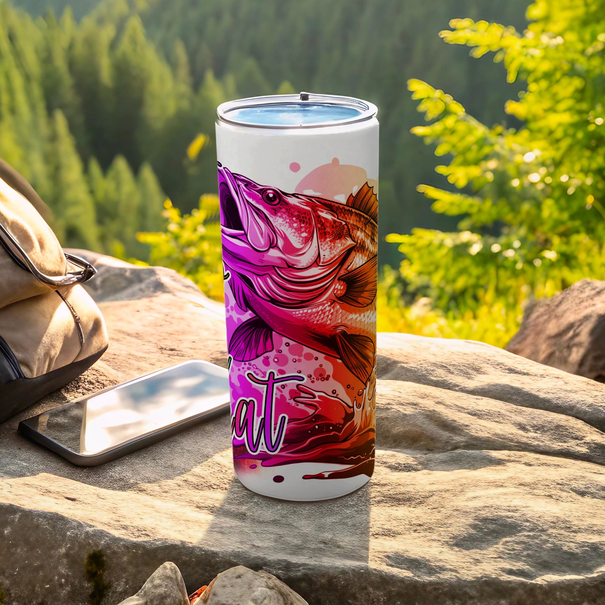 Tumbler with a bass fish and "Fish" text design, placed on rocks outdoors.