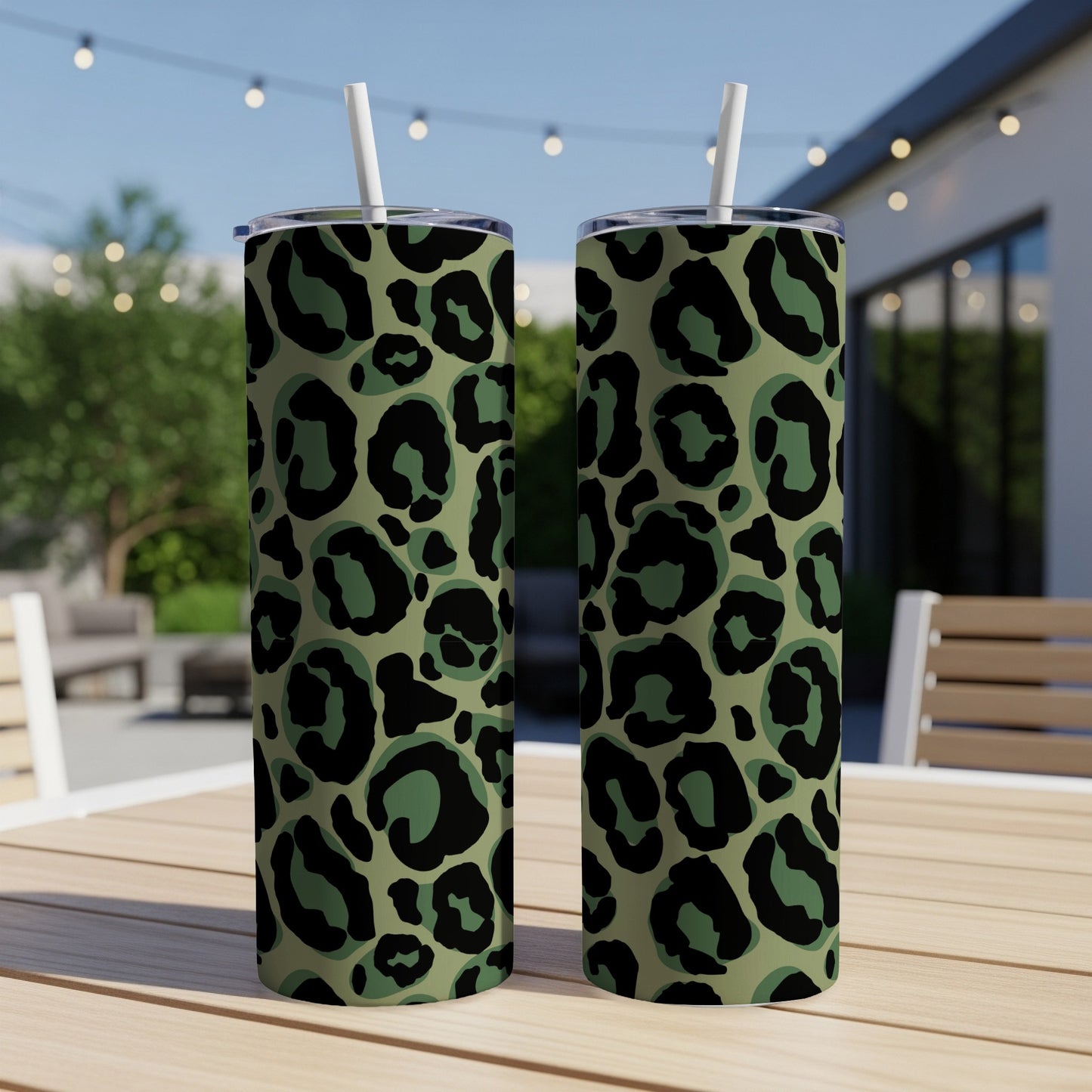 Two tumblers with green and black leopard print and white straws on a wooden table.