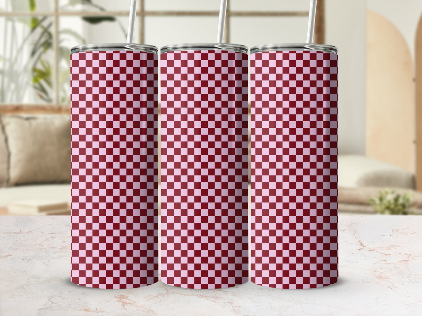 Three pink and maroon checkered tumblers with straws on a marble surface.
