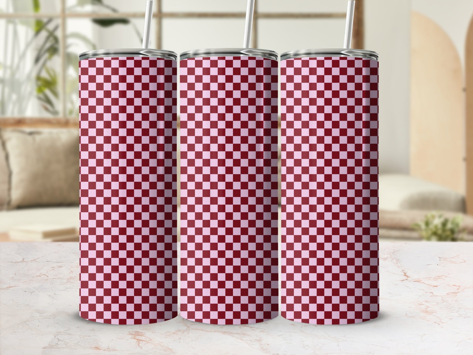 Three pink and maroon checkered tumblers with straws on a marble surface.