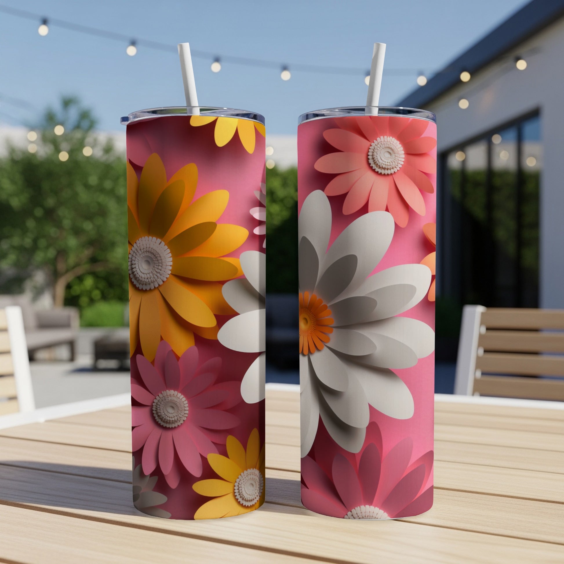 Two pink tumblers with large floral designs sit on a wooden table outdoors.