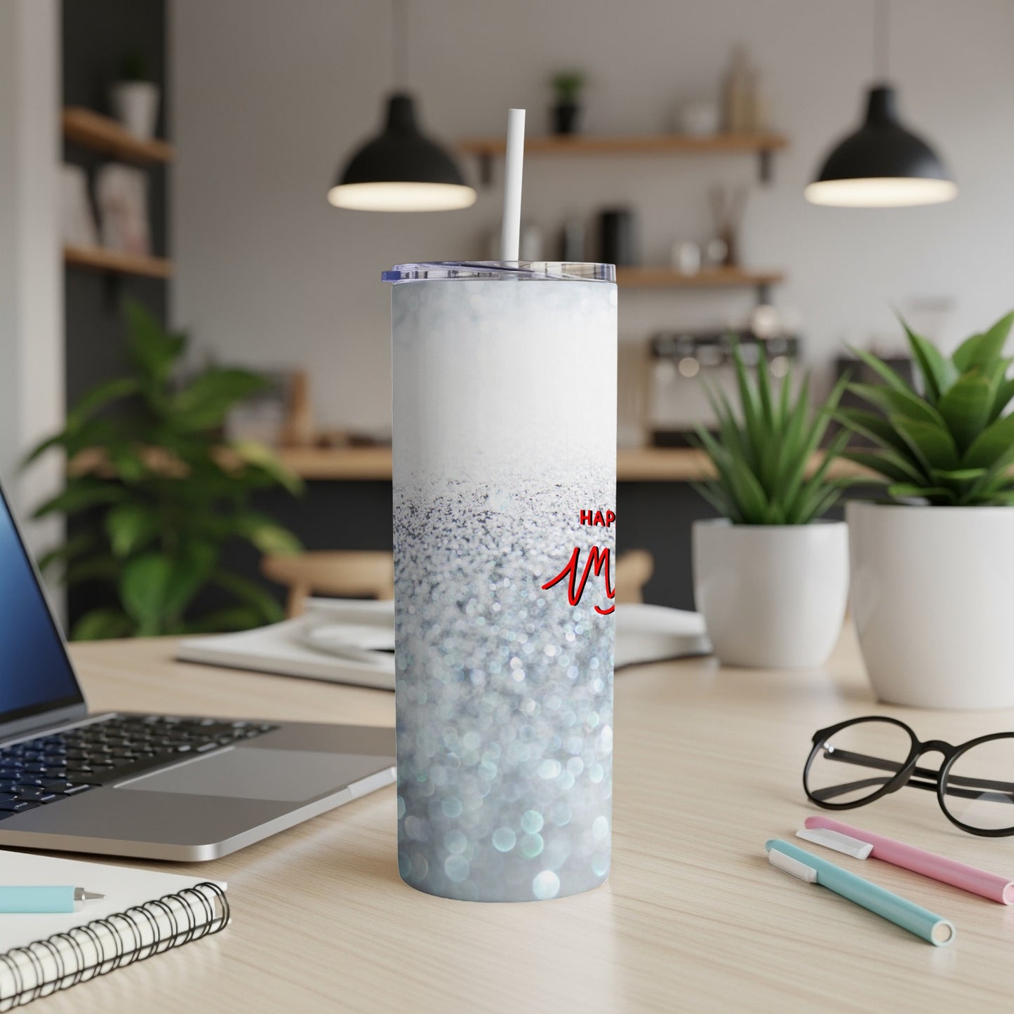 White tumbler with blue glitter and "Happy Mom" text on desk.