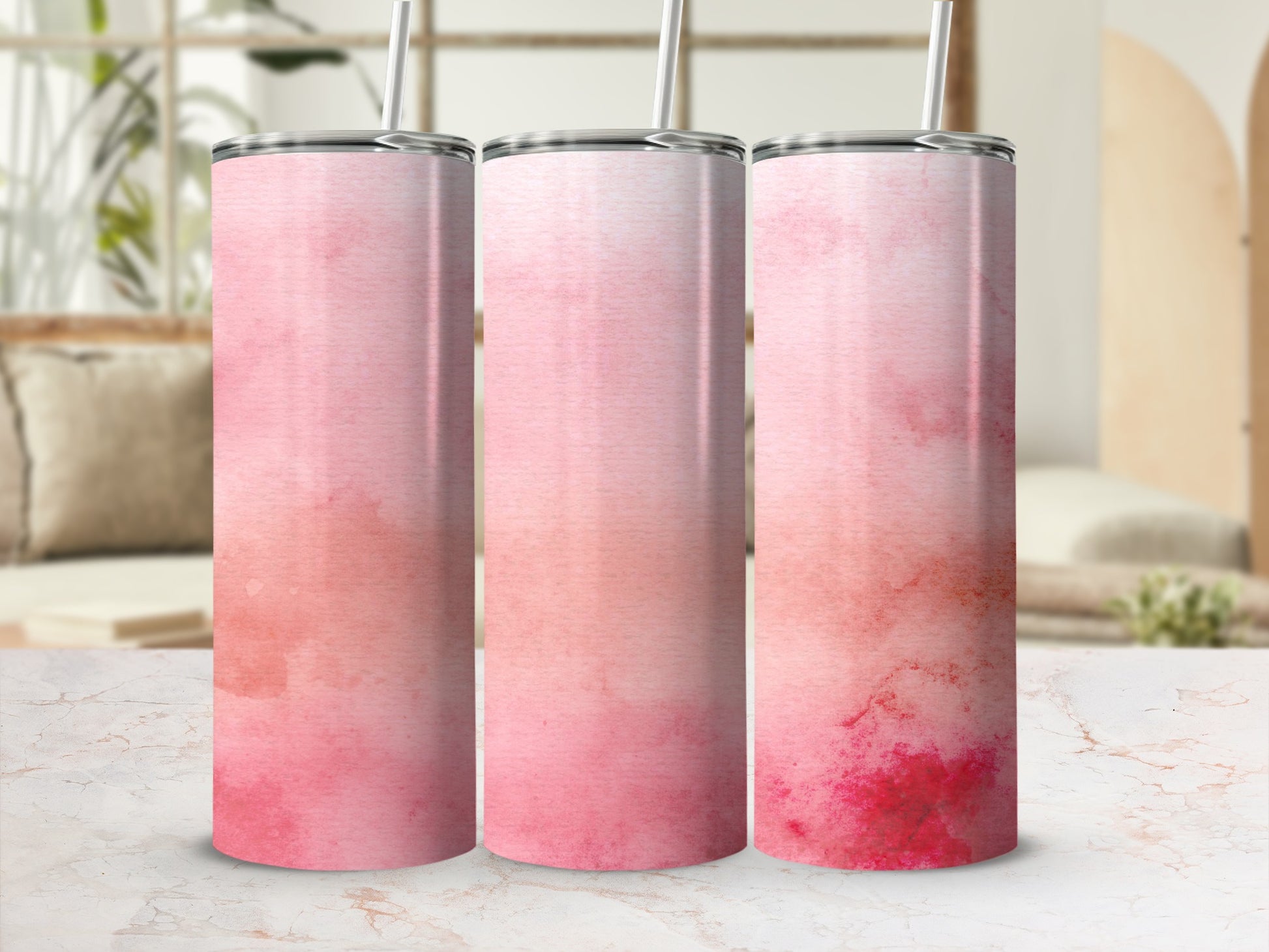 Three pink watercolor tumblers with straws on a marbled surface.