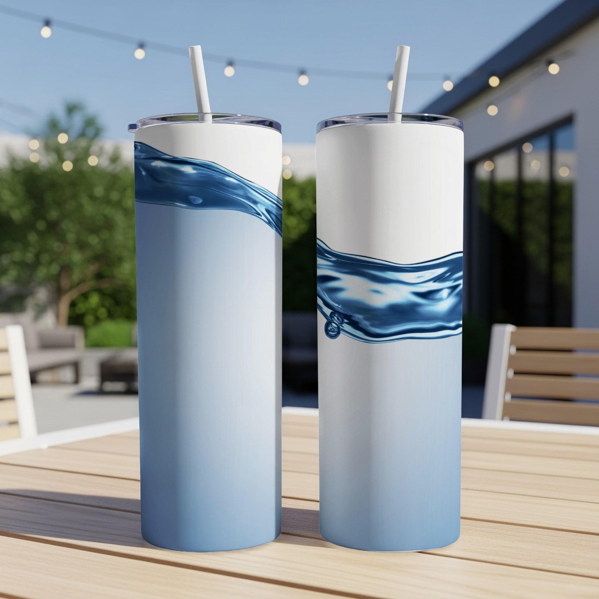 Two white stainless steel tumblers with blue water wave design on outdoor table.