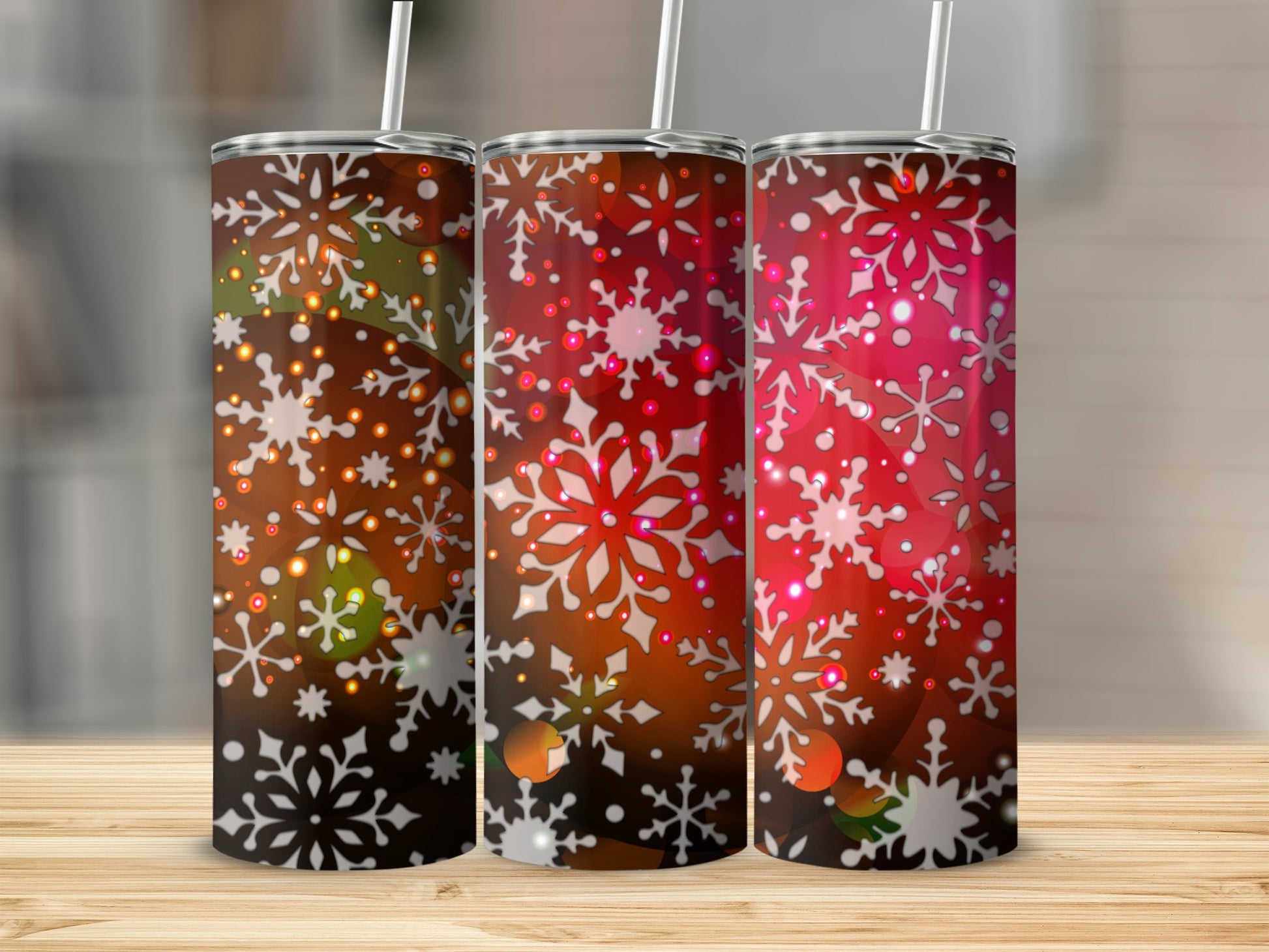 Three tumblers with snowflake designs in red and white on a wooden surface.