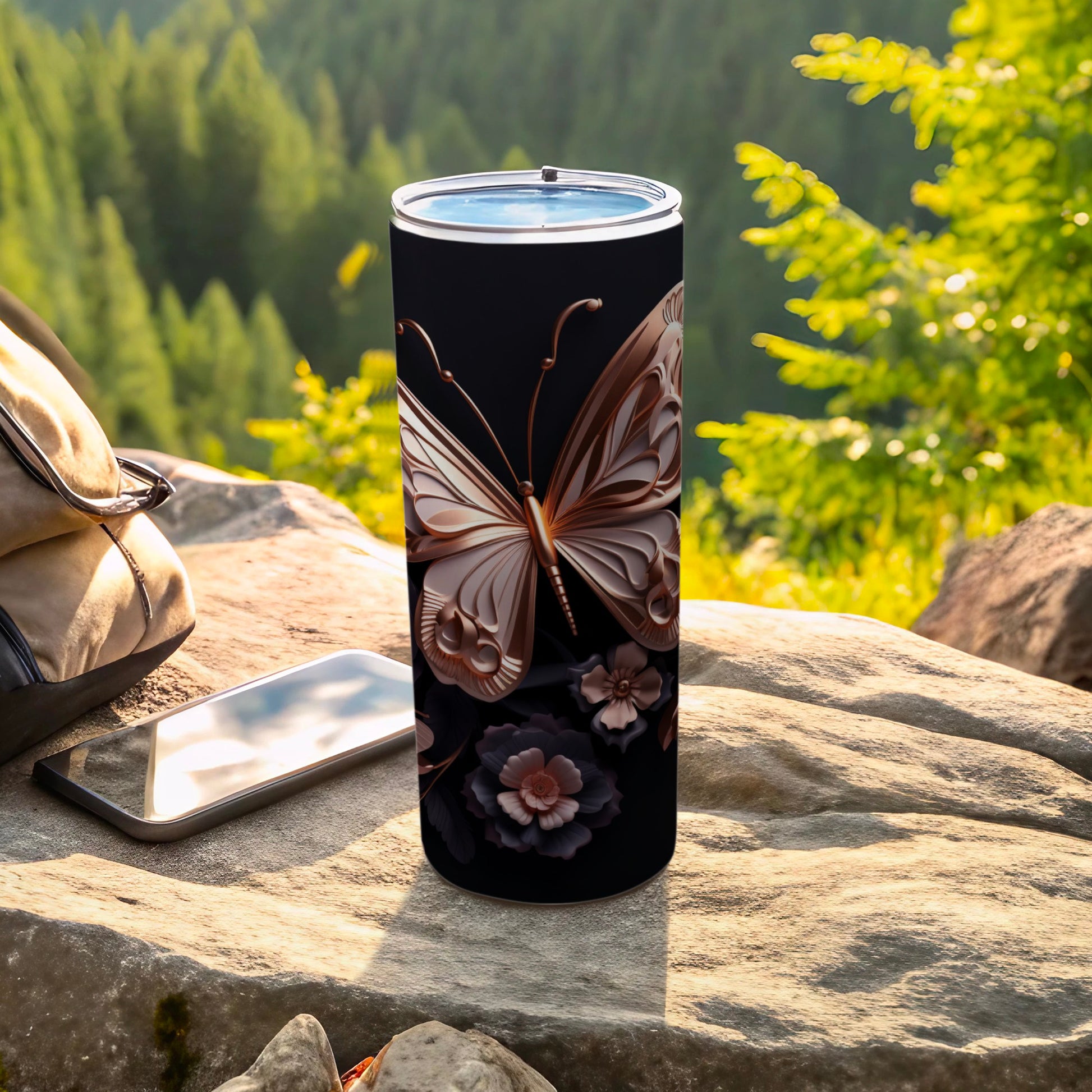 Black tumbler with butterfly and floral design, phone, and bag outdoors.