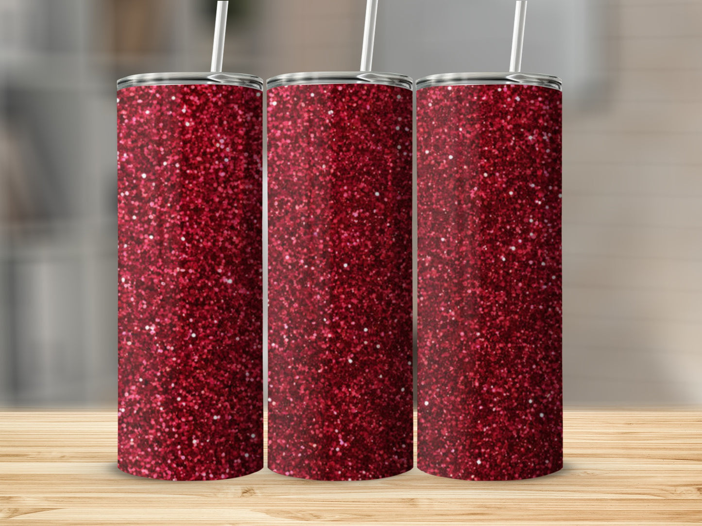 Three glittery red tumblers with white straws on a wooden surface.
