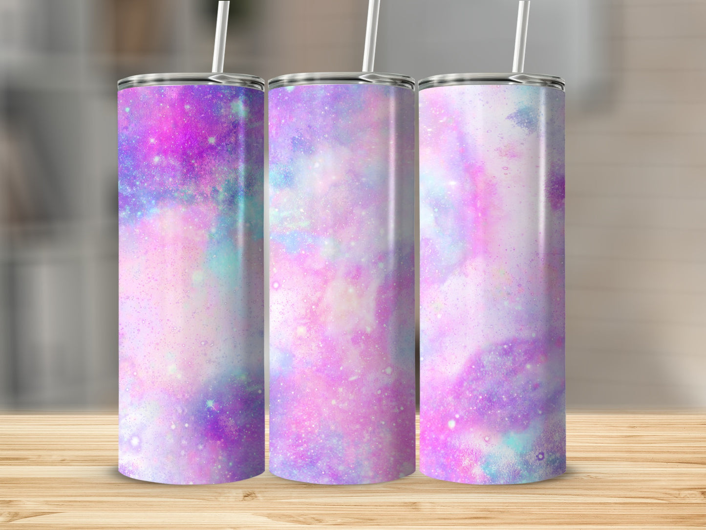 Three iridescent tumblers with galaxy patterns on a wooden surface.