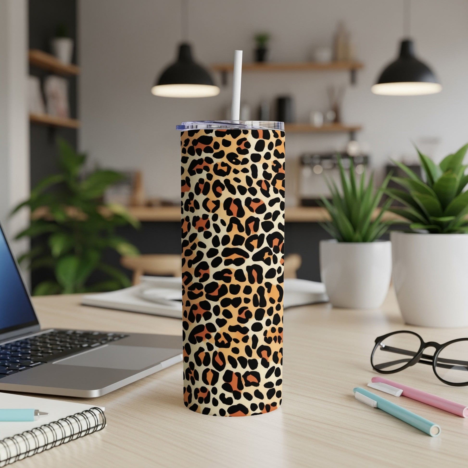 Leopard print tumbler with straw on desk next to laptop and pens.