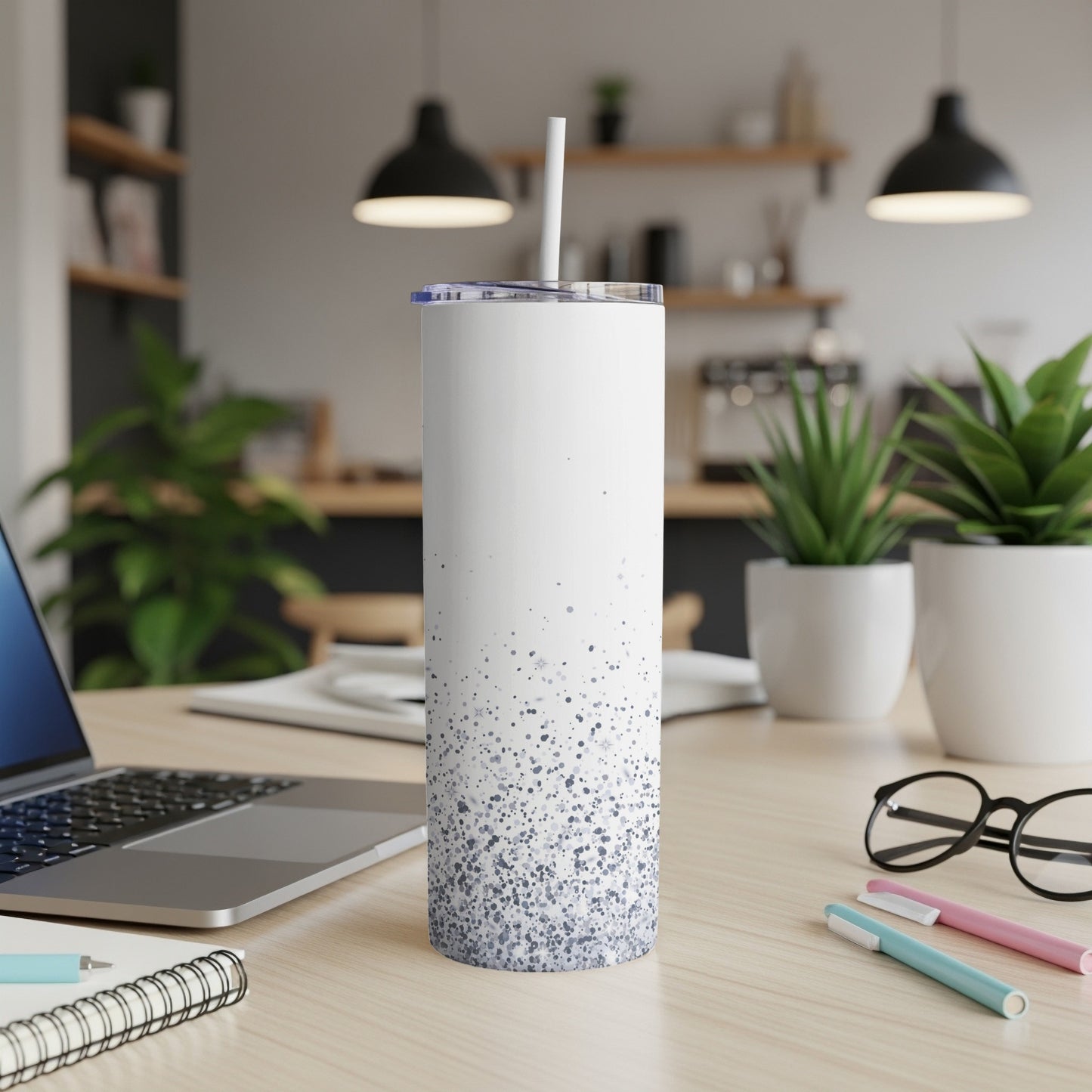 White tumbler with blue speckles, straw, laptop, and pens on desk.
