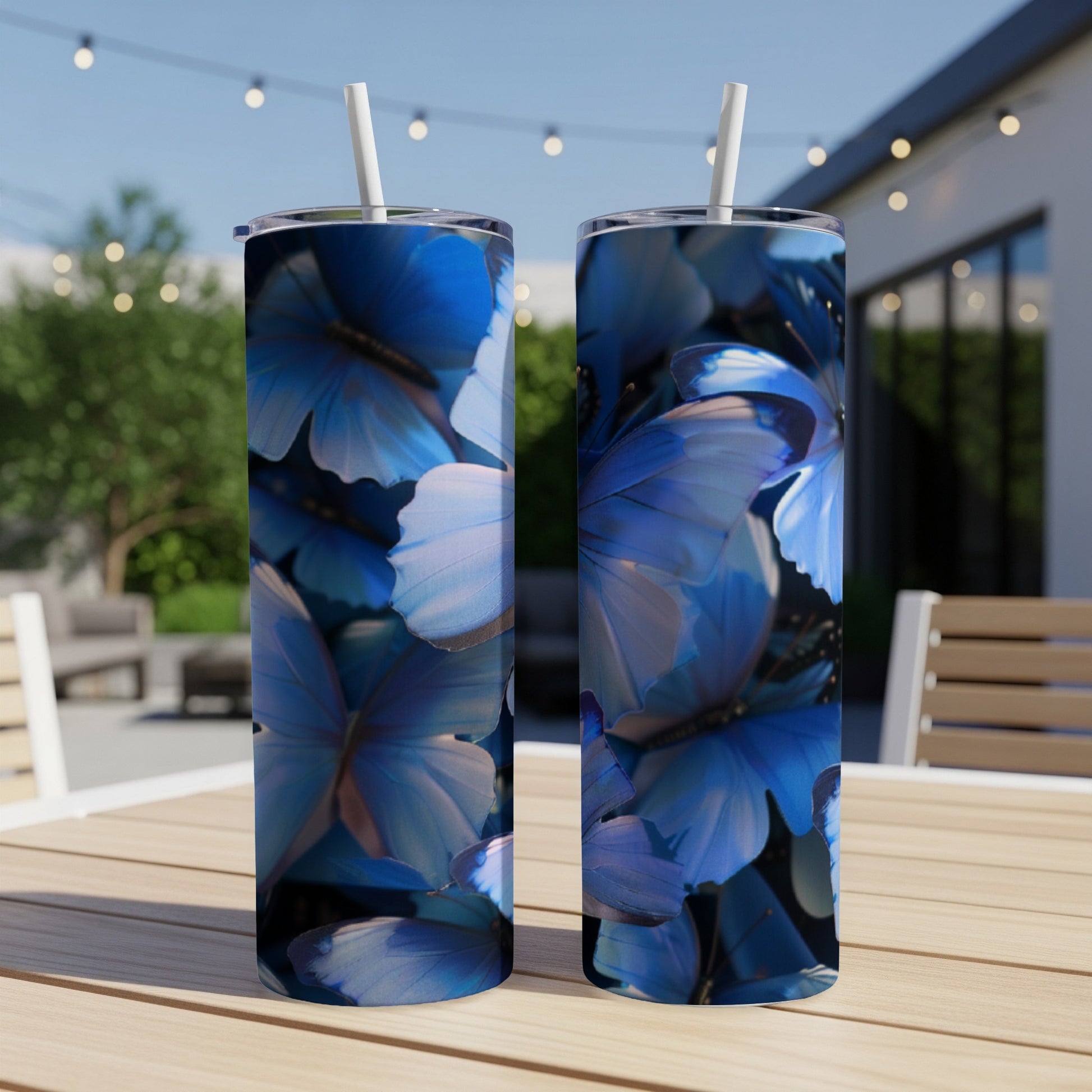 Two blue butterfly pattern tumblers with straws on a wooden table.
