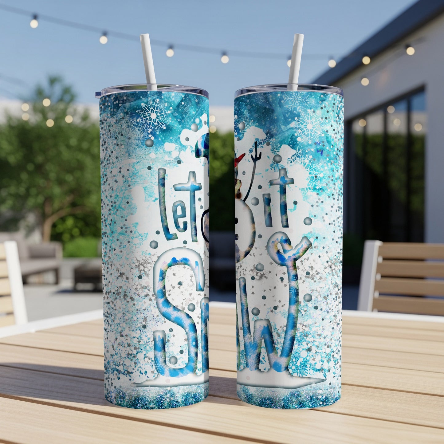 Two tumblers with "Let It Snow" design on an outdoor table.
