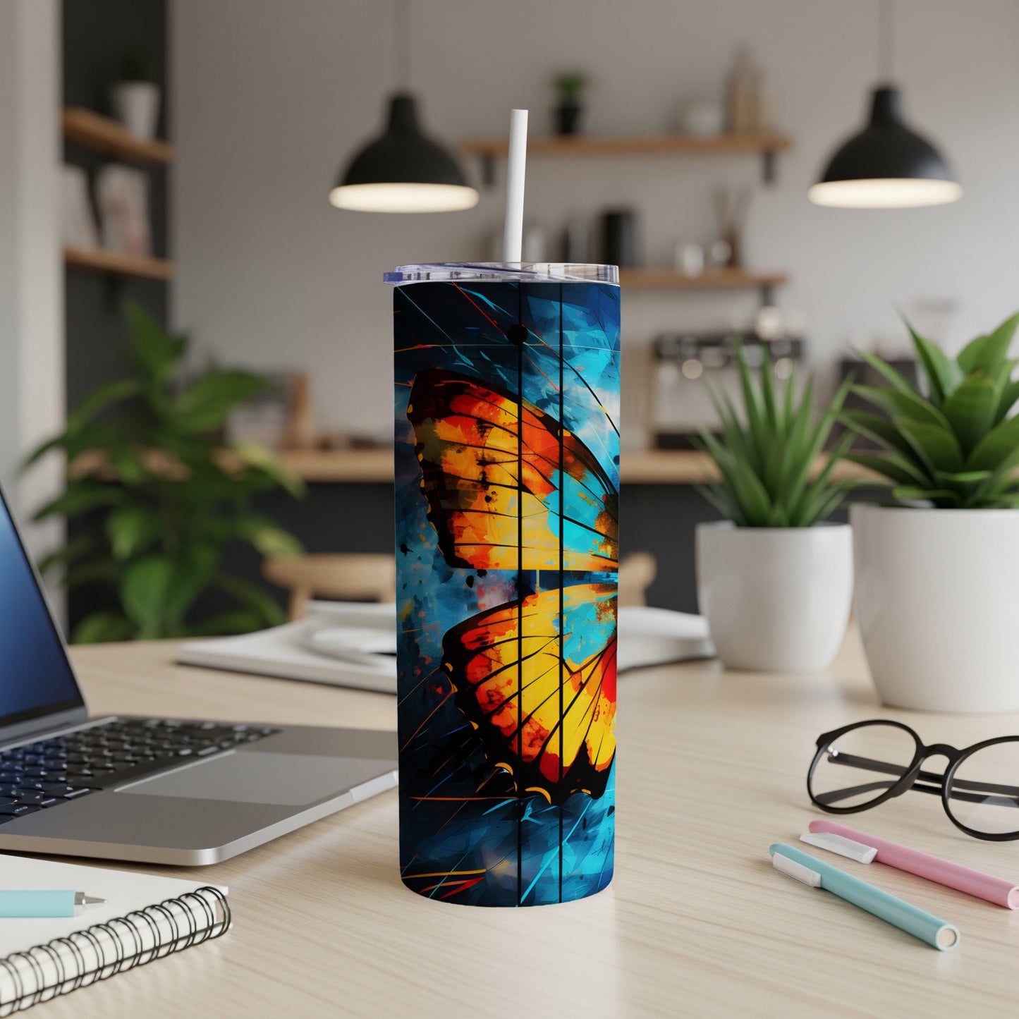 Butterfly tumbler with straw on a desk next to a laptop.