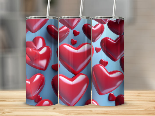 Three shiny red heart-patterned tumblers with straws on a wooden surface.