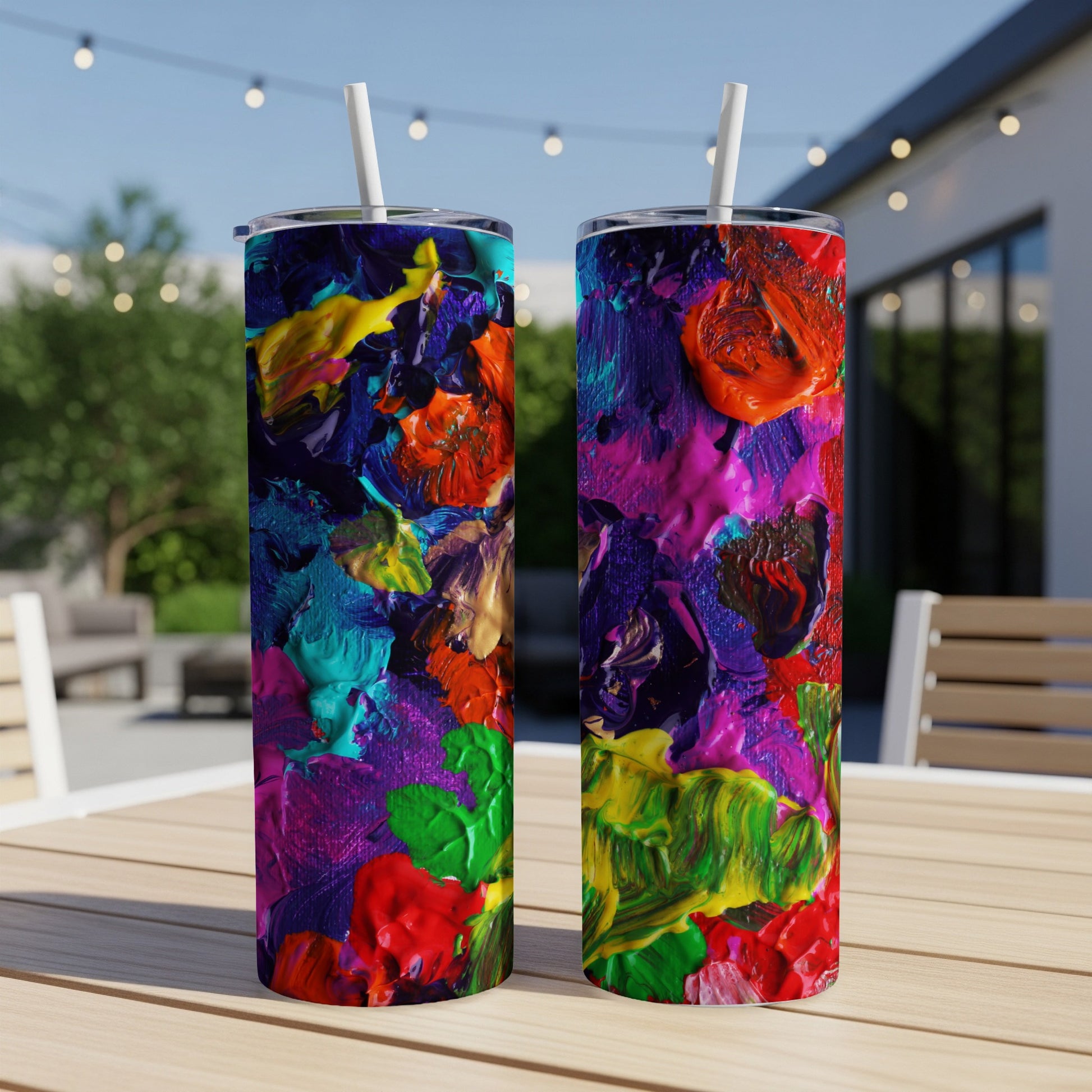 Two tumblers with vibrant, textured, abstract paint designs on a wooden table.