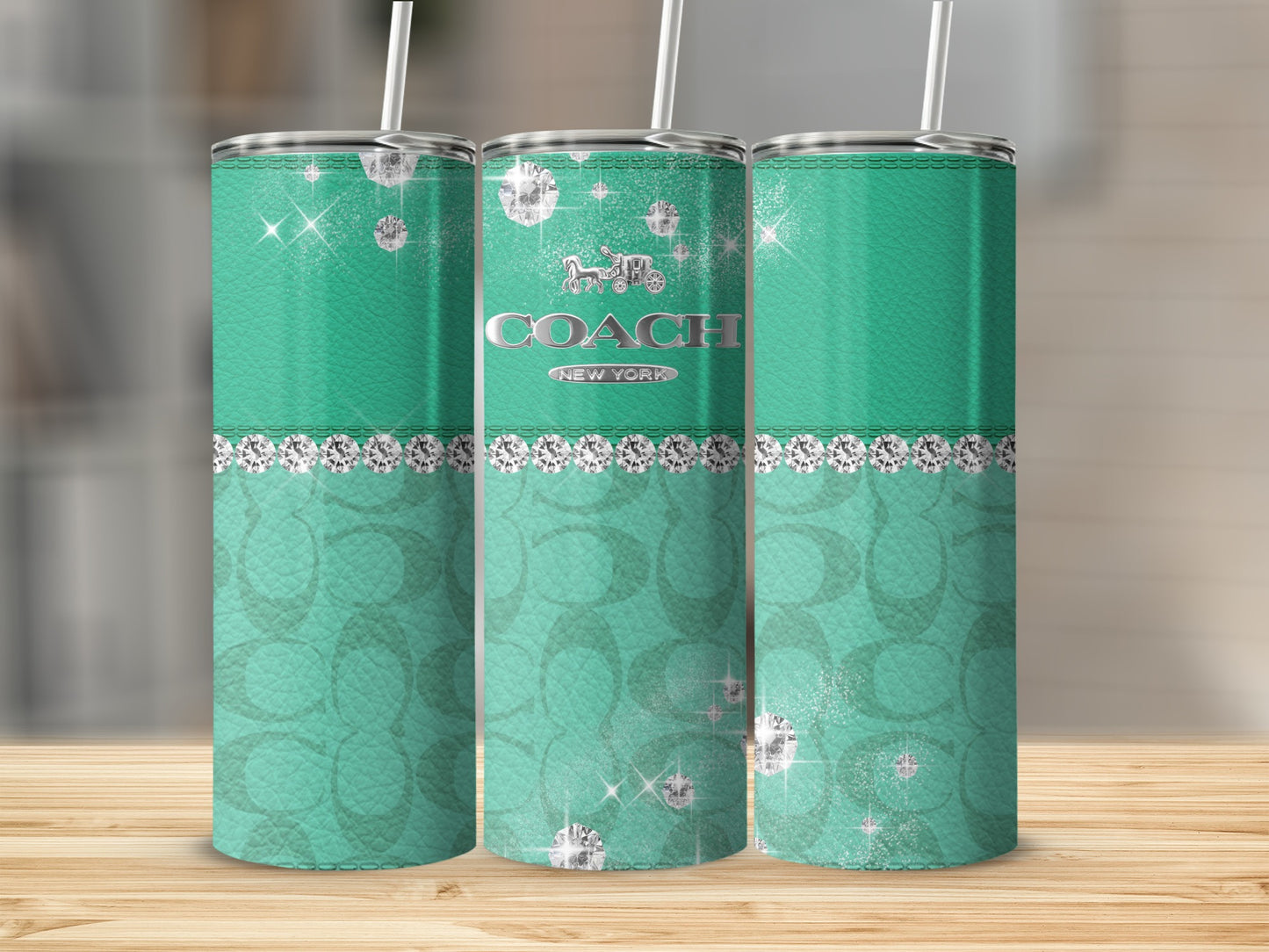 Three turquoise tumblers with diamonds and Coach logo on a wooden surface.